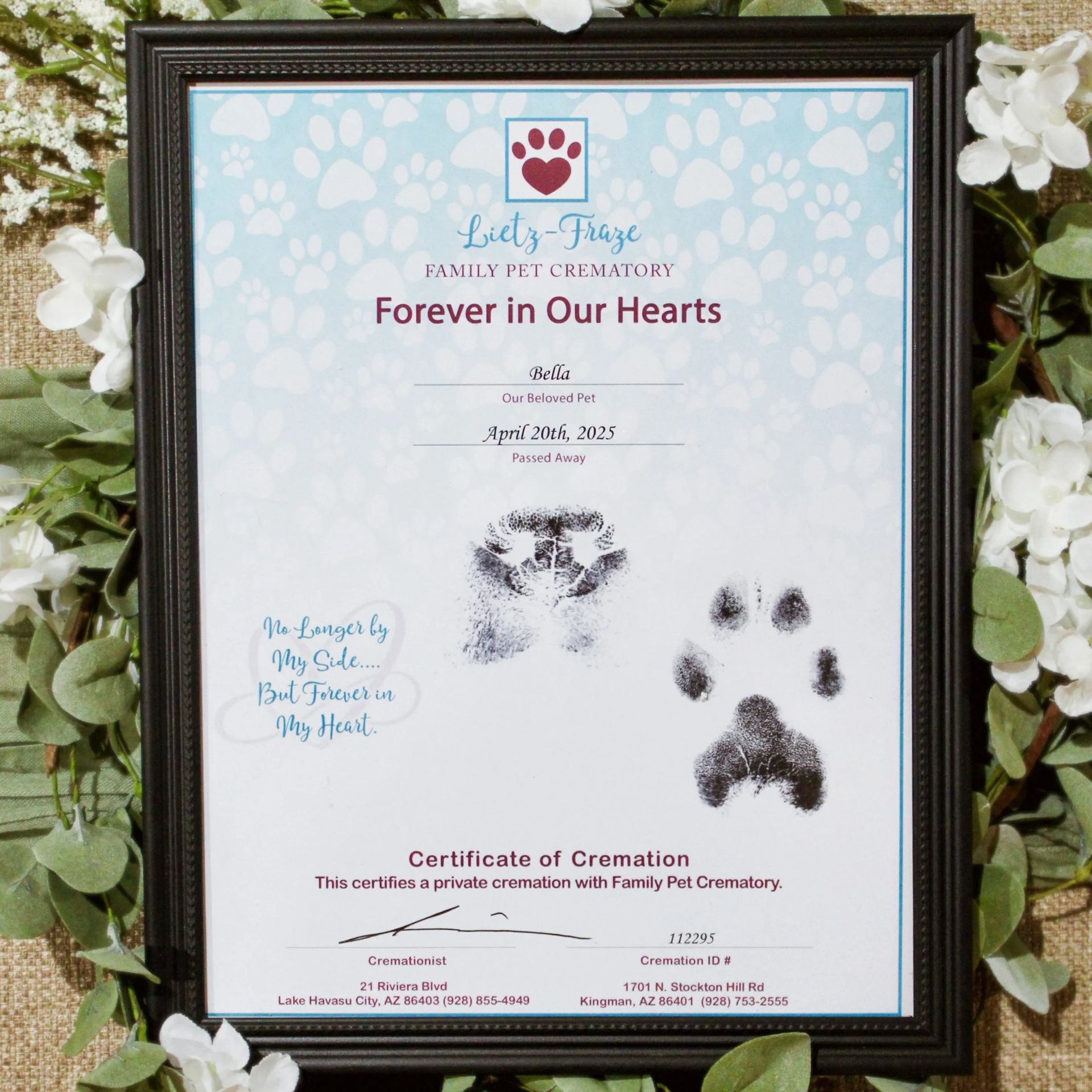 Framed pet memorial certificate with paw prints and floral decorations on a light background