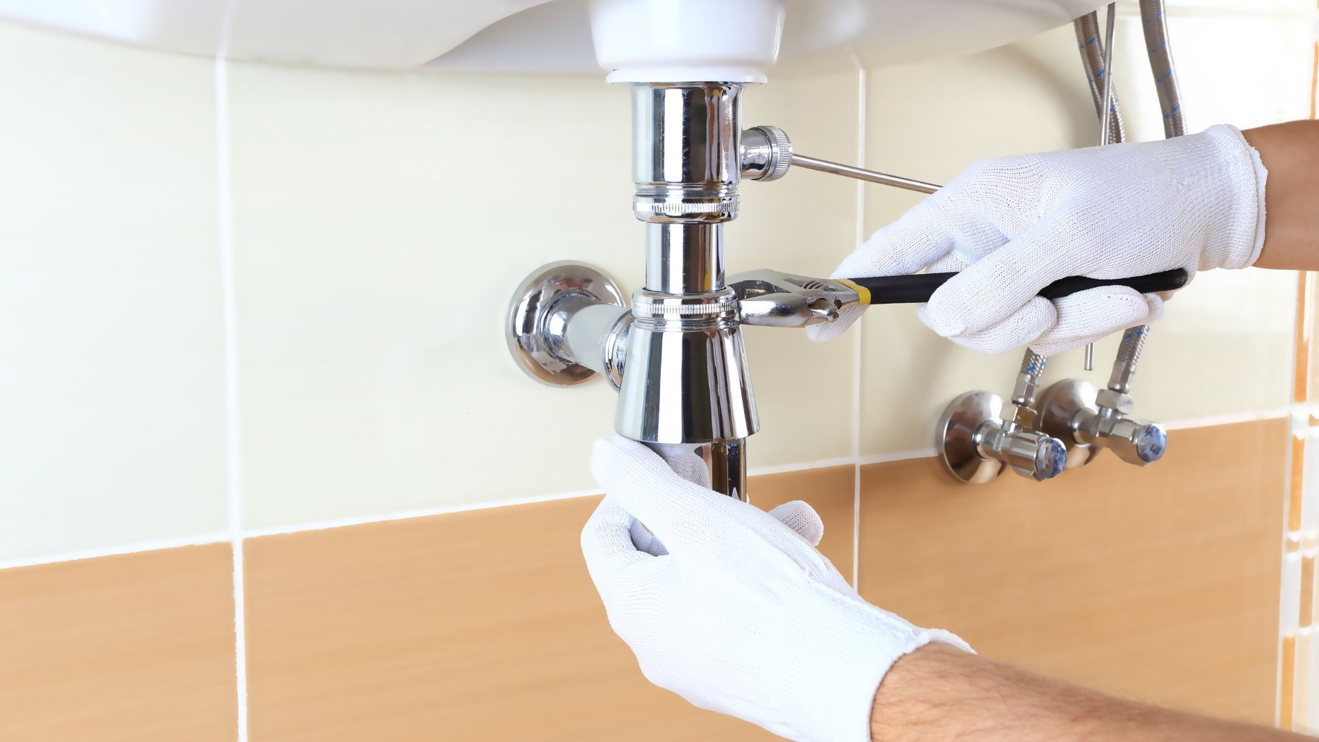 A plumber is fixing a sink pipe with a wrench.