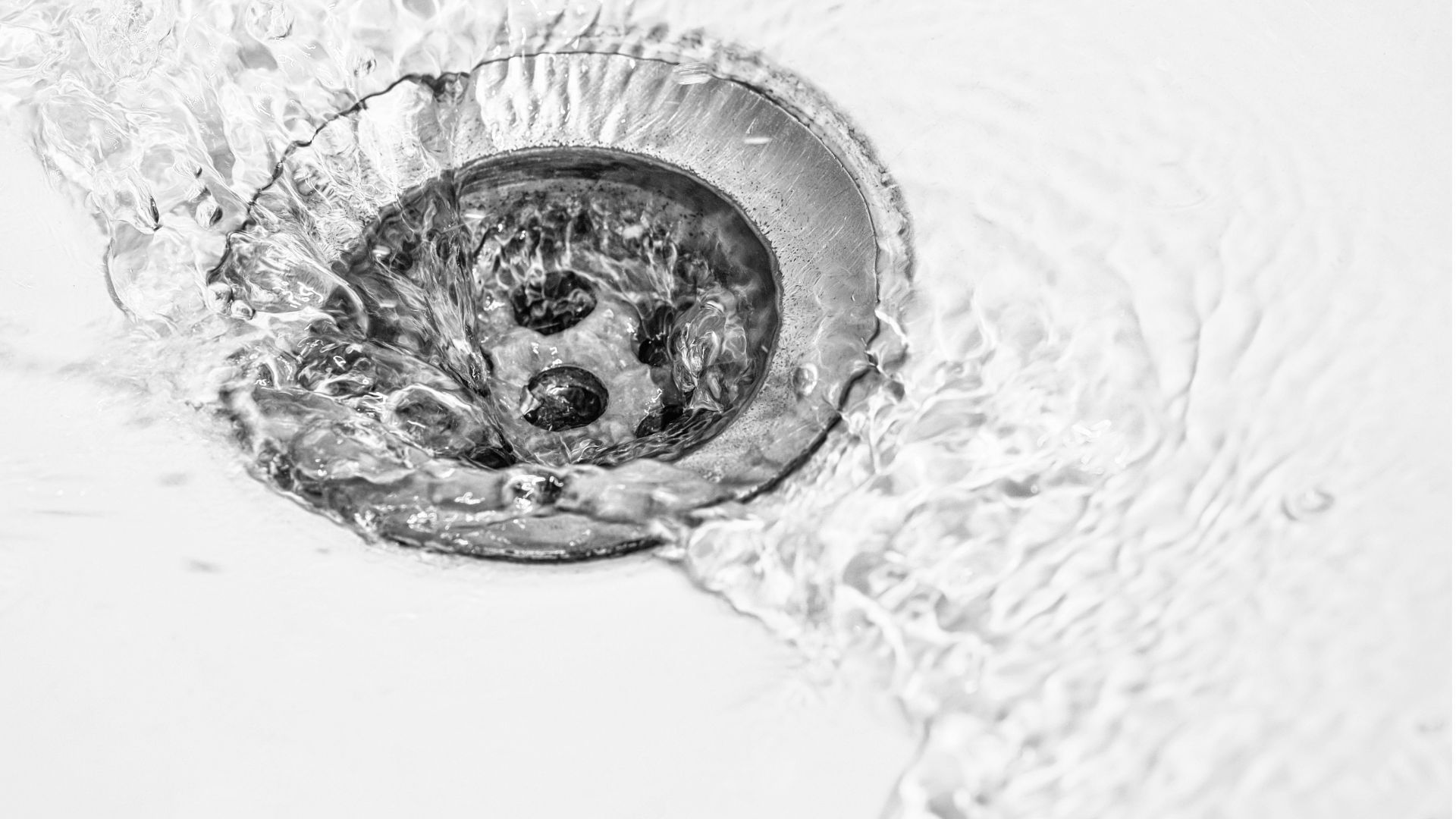 A black and white photo of water running down a sink drain.