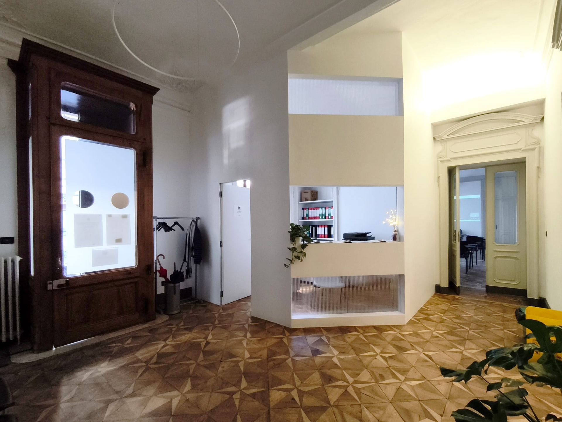 Ingresso decorato con pavimenti in legno, alta porta scura e una moderna parete bianca angolare.