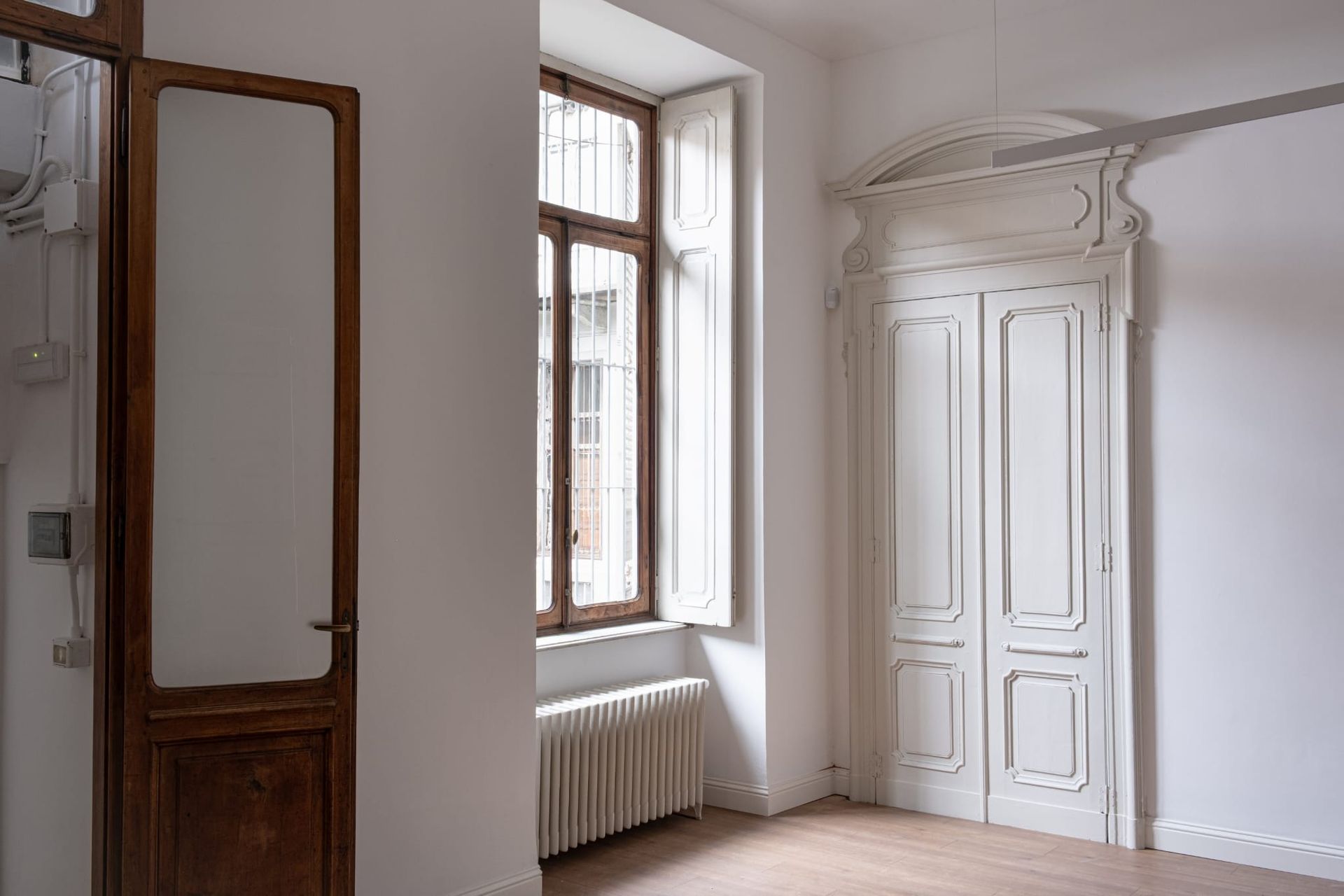 Vista interna con porta in legno, finestra e doppie porte bianche chiuse. Le pareti sono bianche.