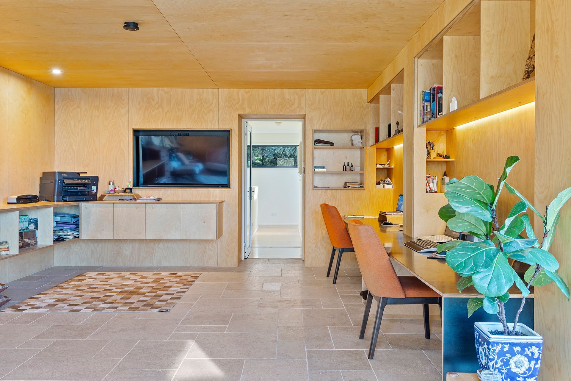 A living room with a desk , chairs , a television and a potted plant.