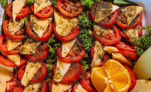 Tomates en rodajas, patatas y hierbas aromáticas en una bandeja con gajos de naranja y perejil picado.