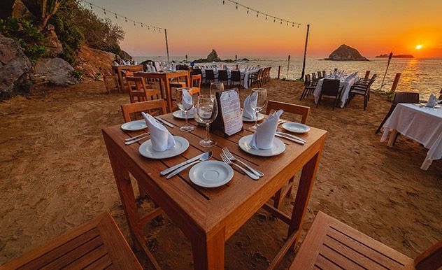 Mesa de comedor frente al mar puesta al atardecer, con vistas al océano y un cielo de un cálido color naranja.