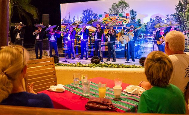 Los músicos actúan en un escenario al aire libre mientras los comensales observan desde las mesas situadas en primer plano.
