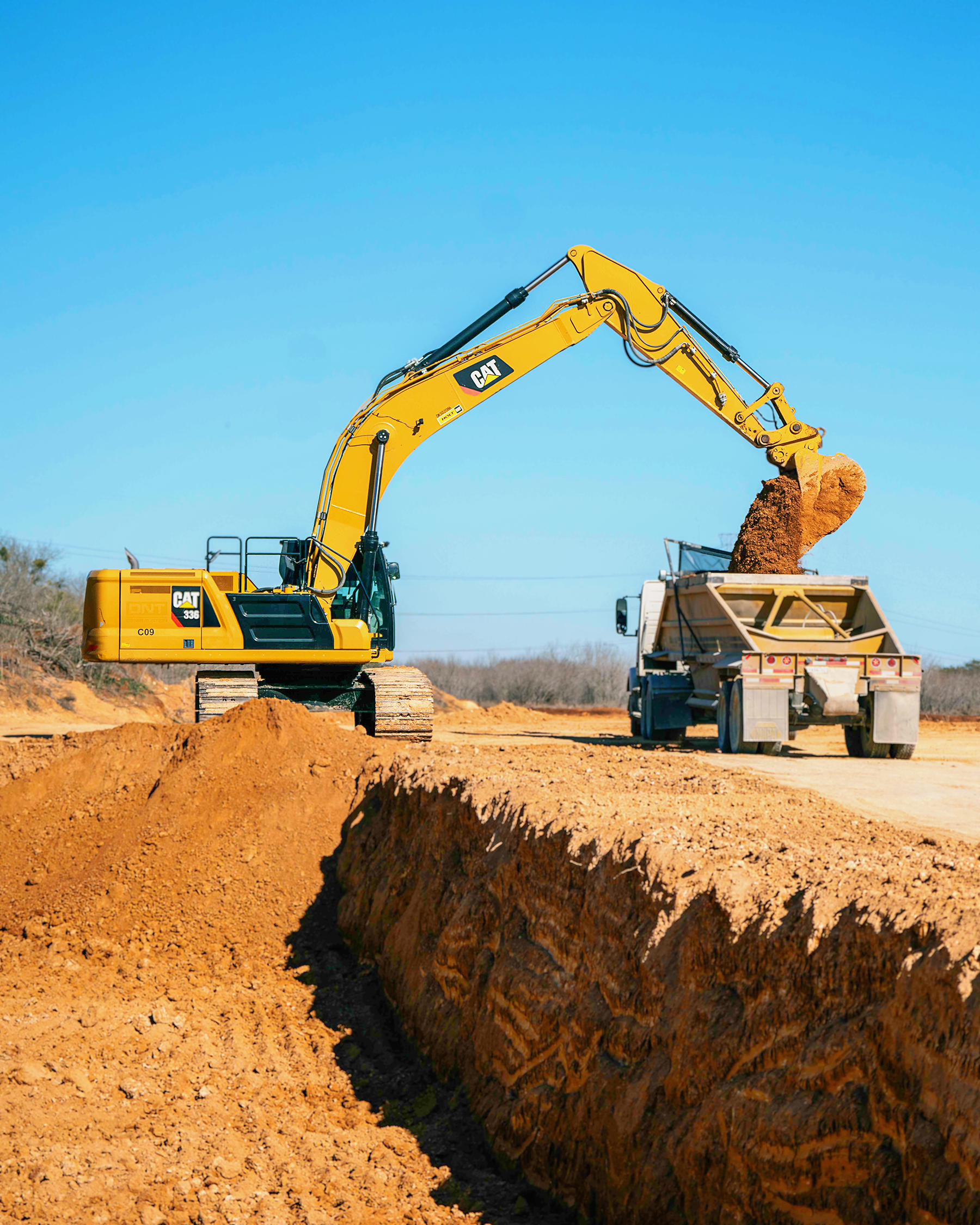 An aerial view of three construction vehicles on a dirt road.