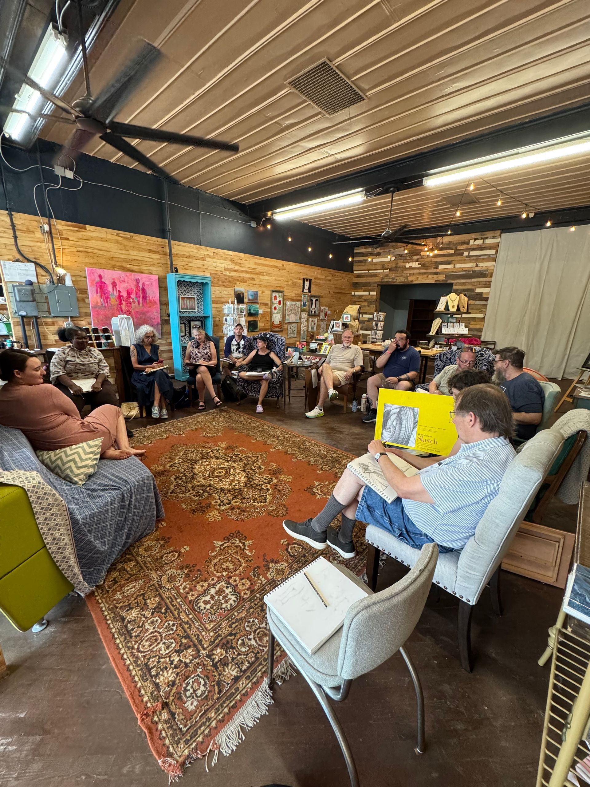 People seated in a cozy studio gathering, with guitars, artwork, and microphones in the background
