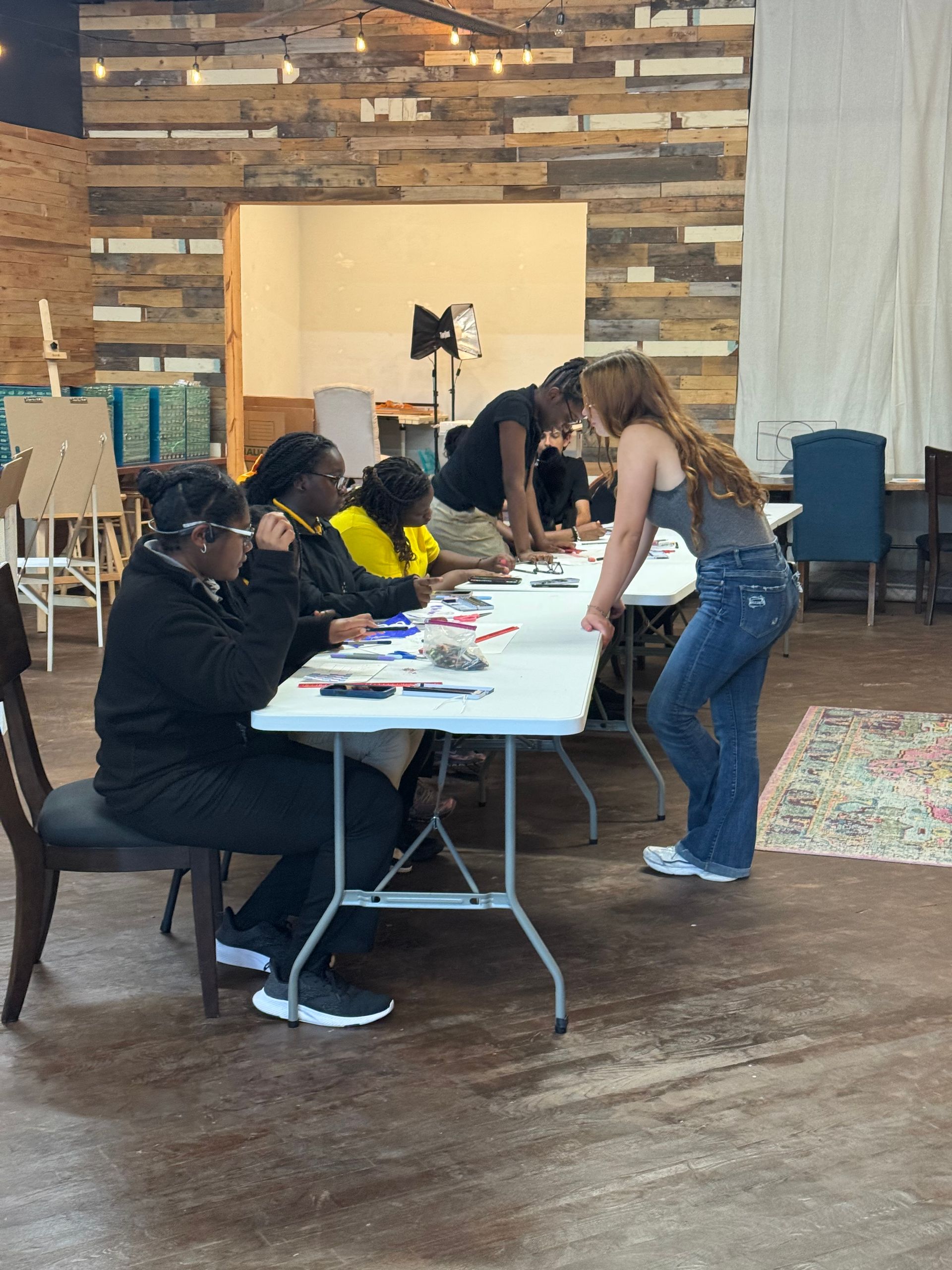 People seated at a table with papers while a woman leans over to help in a community room