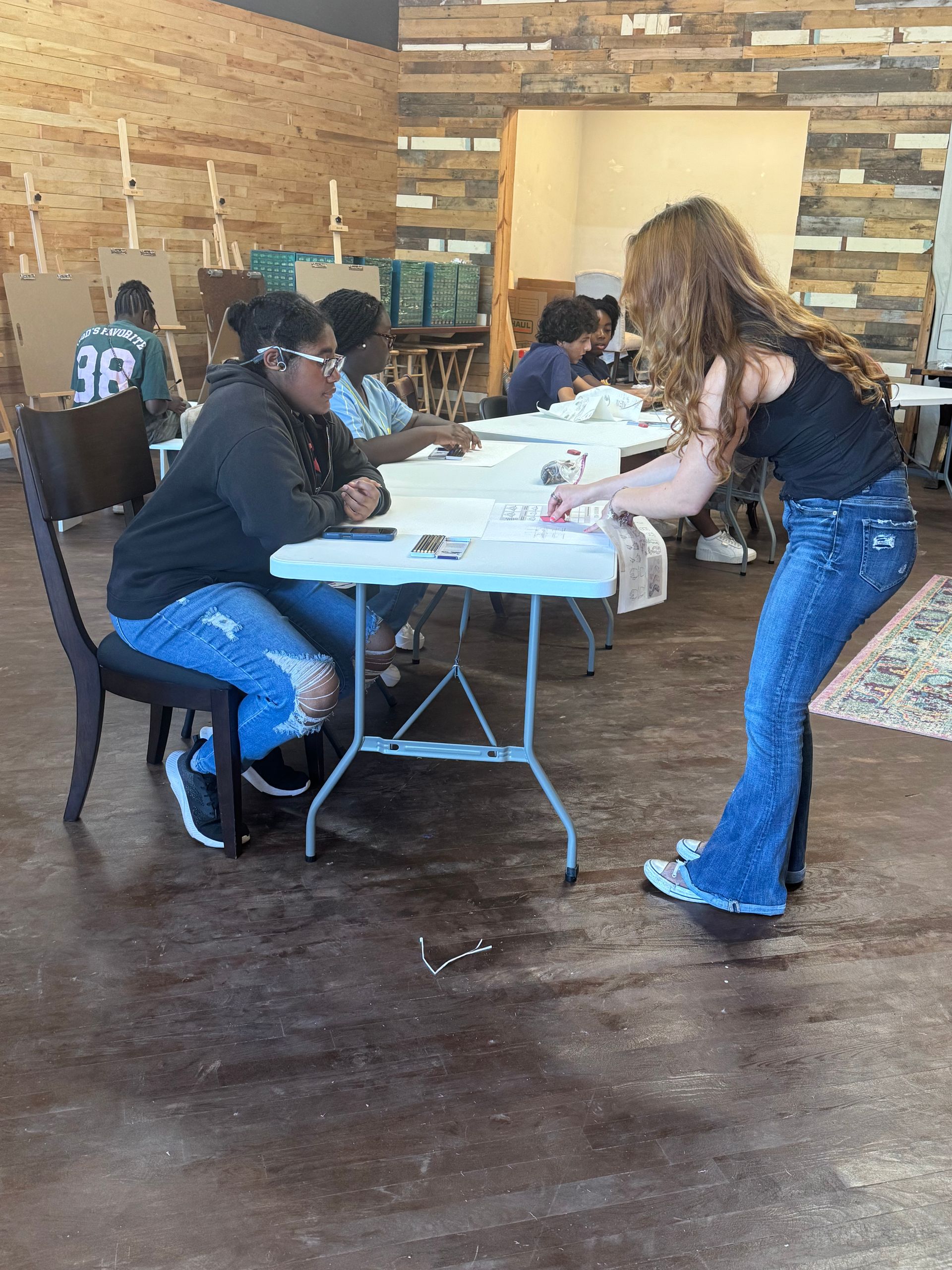 People at tables in a rustic room, with one person handing out items to seated attendees.