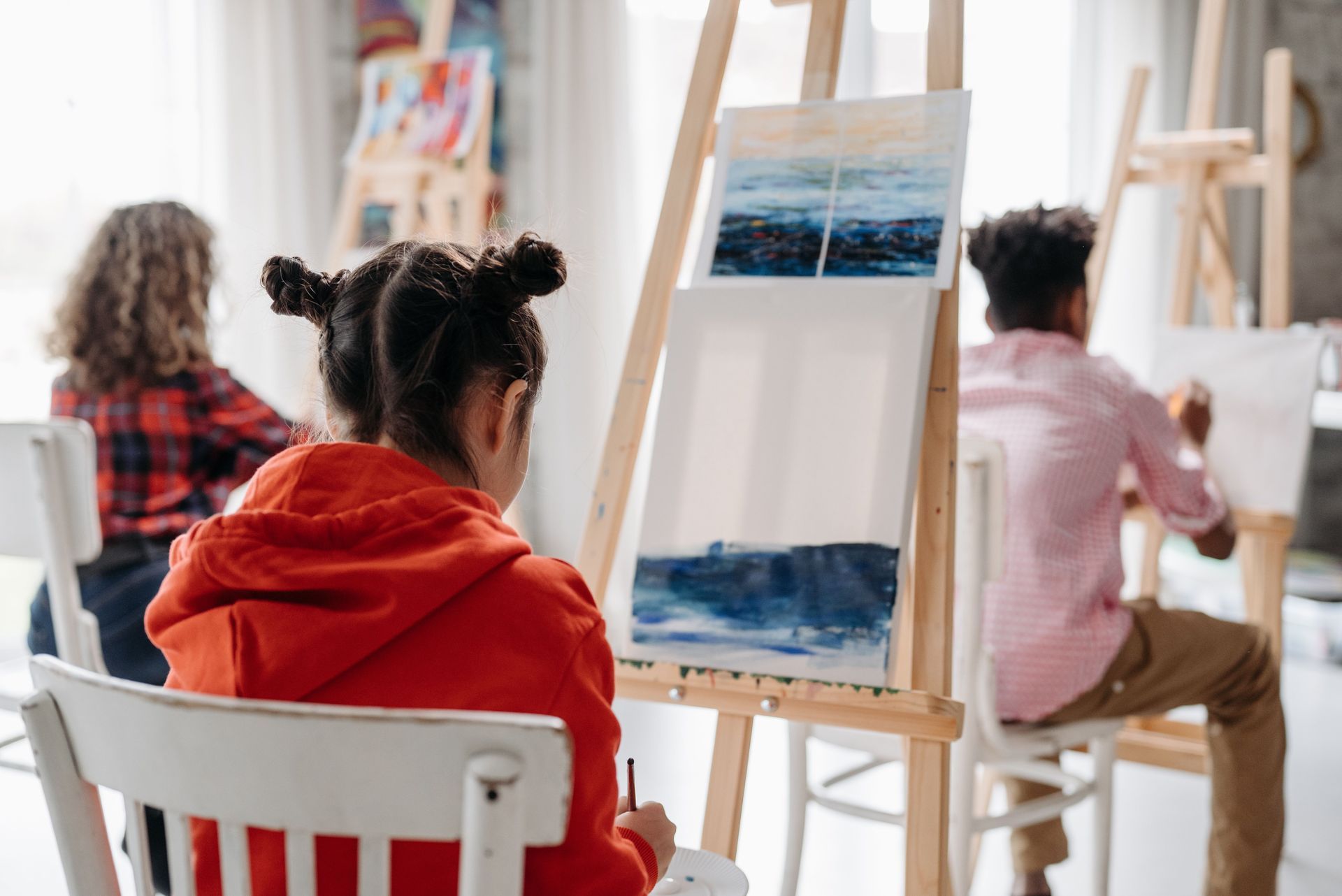 Art class with three people painting at easels in a bright studio