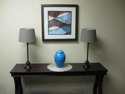 Console table with blue vase, framed abstract art, and two gray lamps against a beige wall