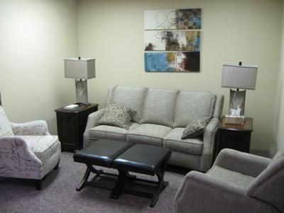 Living room with gray sofa, armchairs, lamps, and coffee table against a light wall.