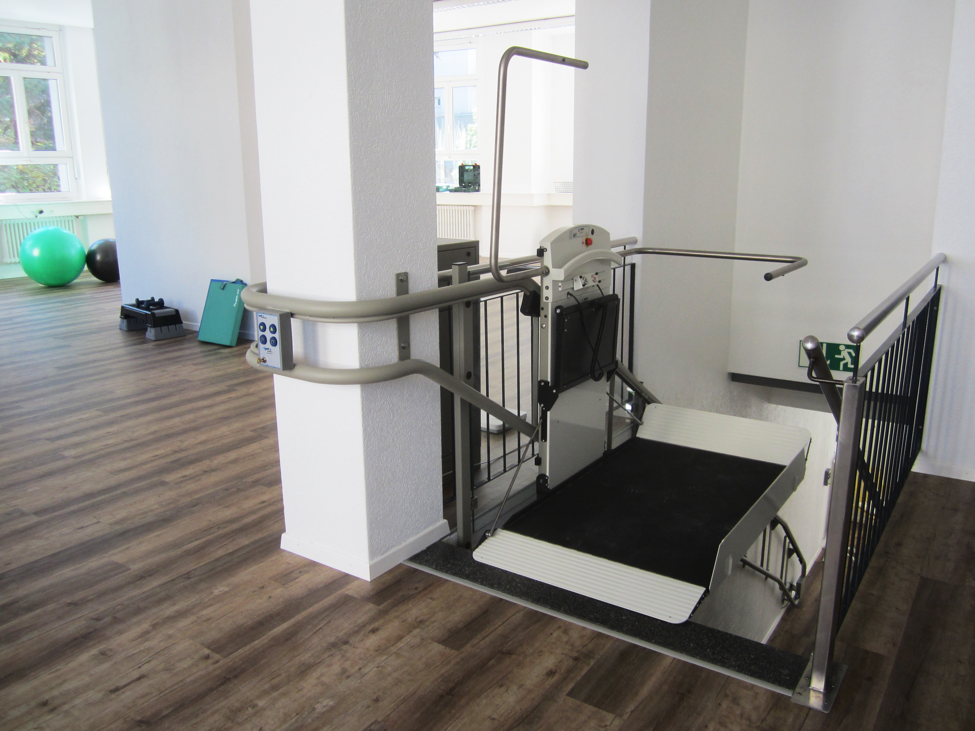 Wheelchair lift deployed from white van, lifting a wheelchair at a building entrance.