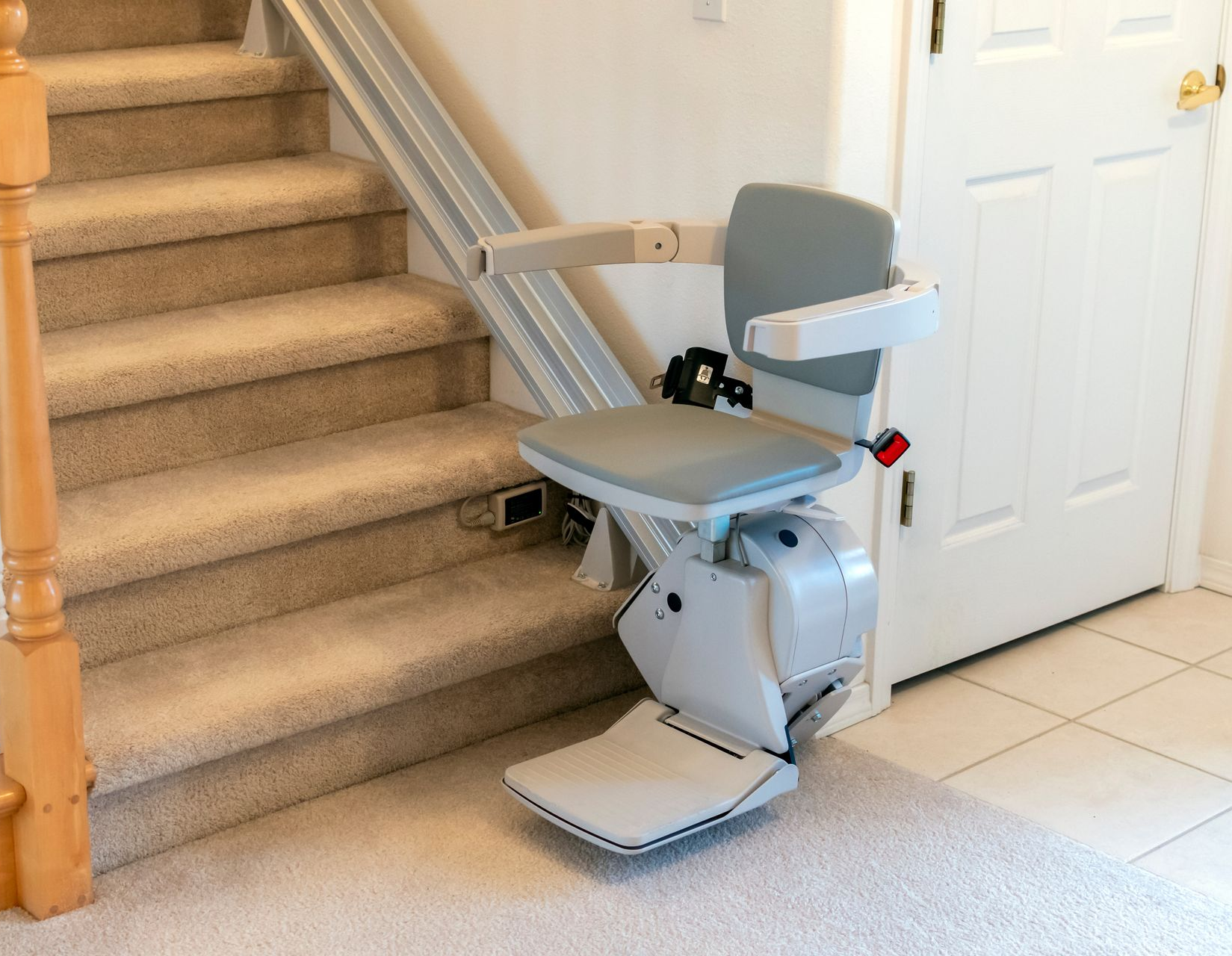 Silver stair lift beside beige carpeted stairs and a white door in a home entryway.