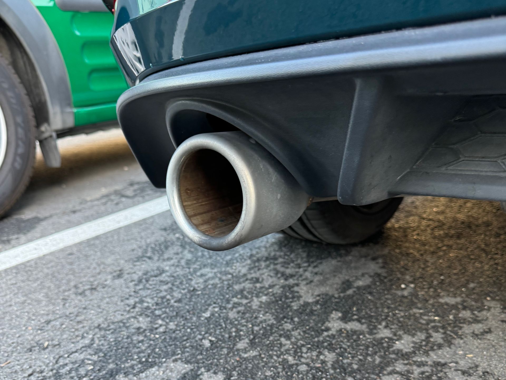 A close up of a car exhaust pipe in a parking lot.