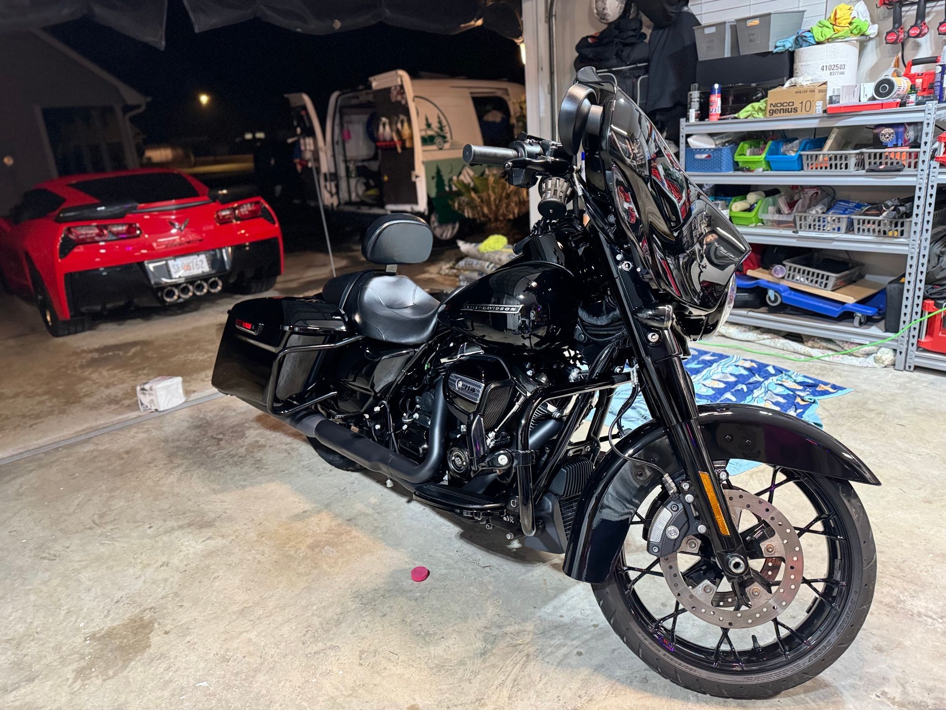 A black motorcycle is parked in a garage next to a red car.