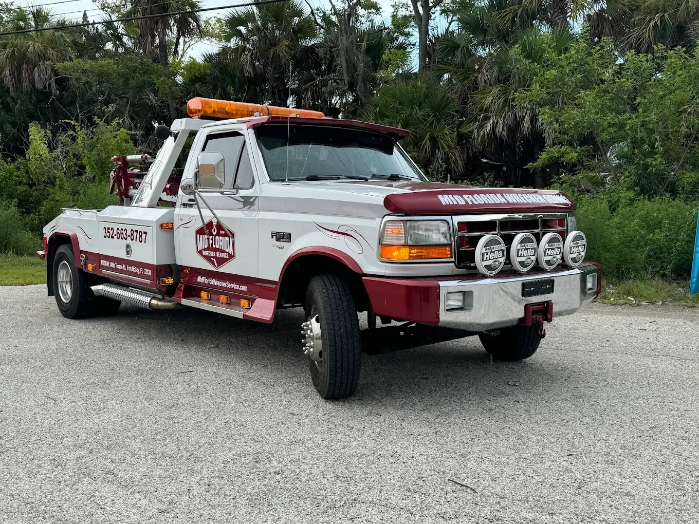 A white and burgundy tow truck parked on gravel.