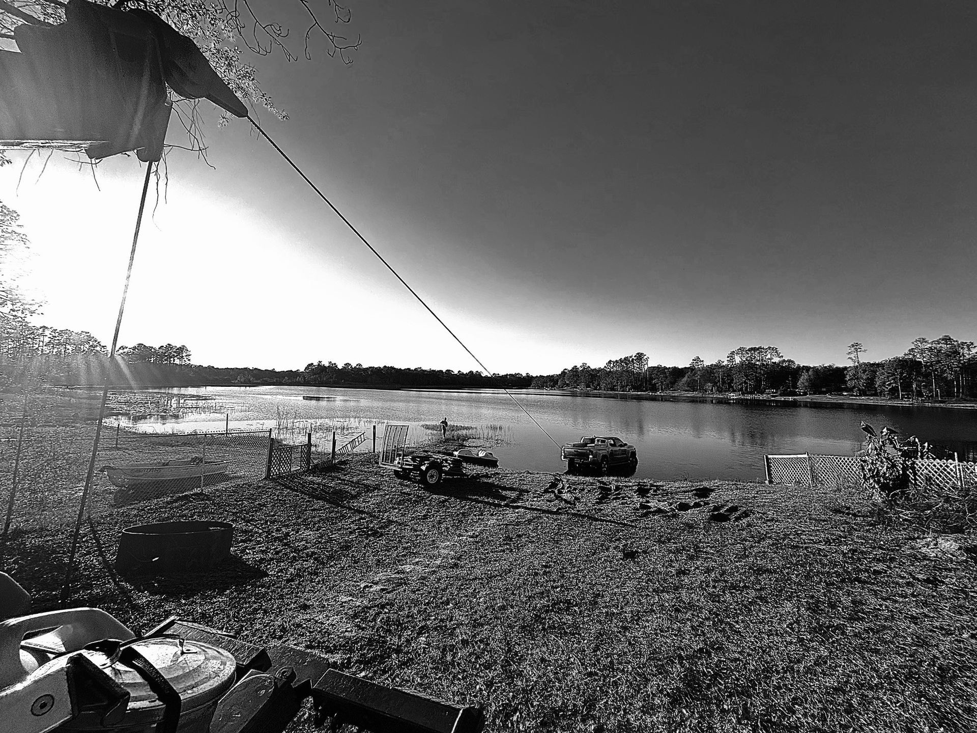 Black and white landscape of a lake with equipment in the foreground, and a person fishing.