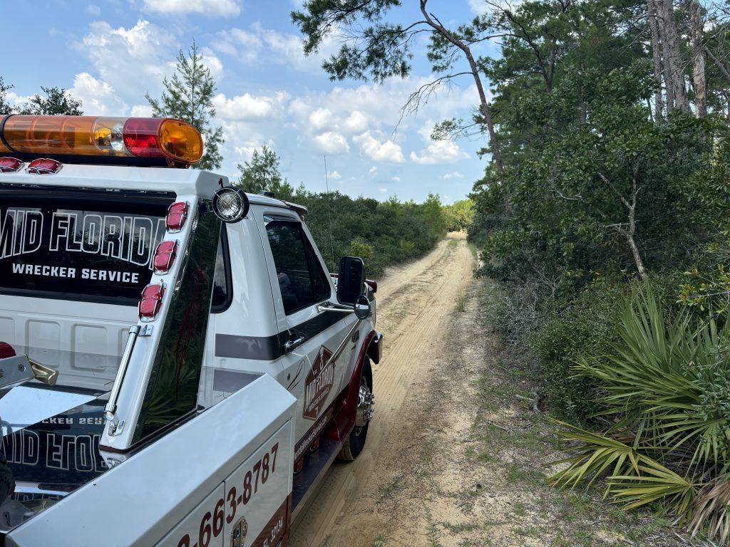 Tow truck on a sandy road in a wooded area with a blue sky.