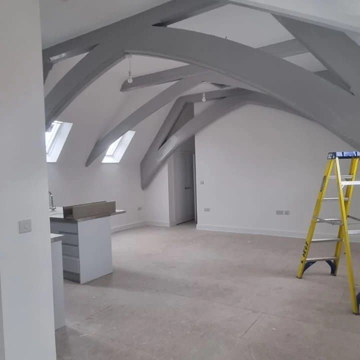 A photo of a room with arched beams painted in dark grey and painted light grey walls.