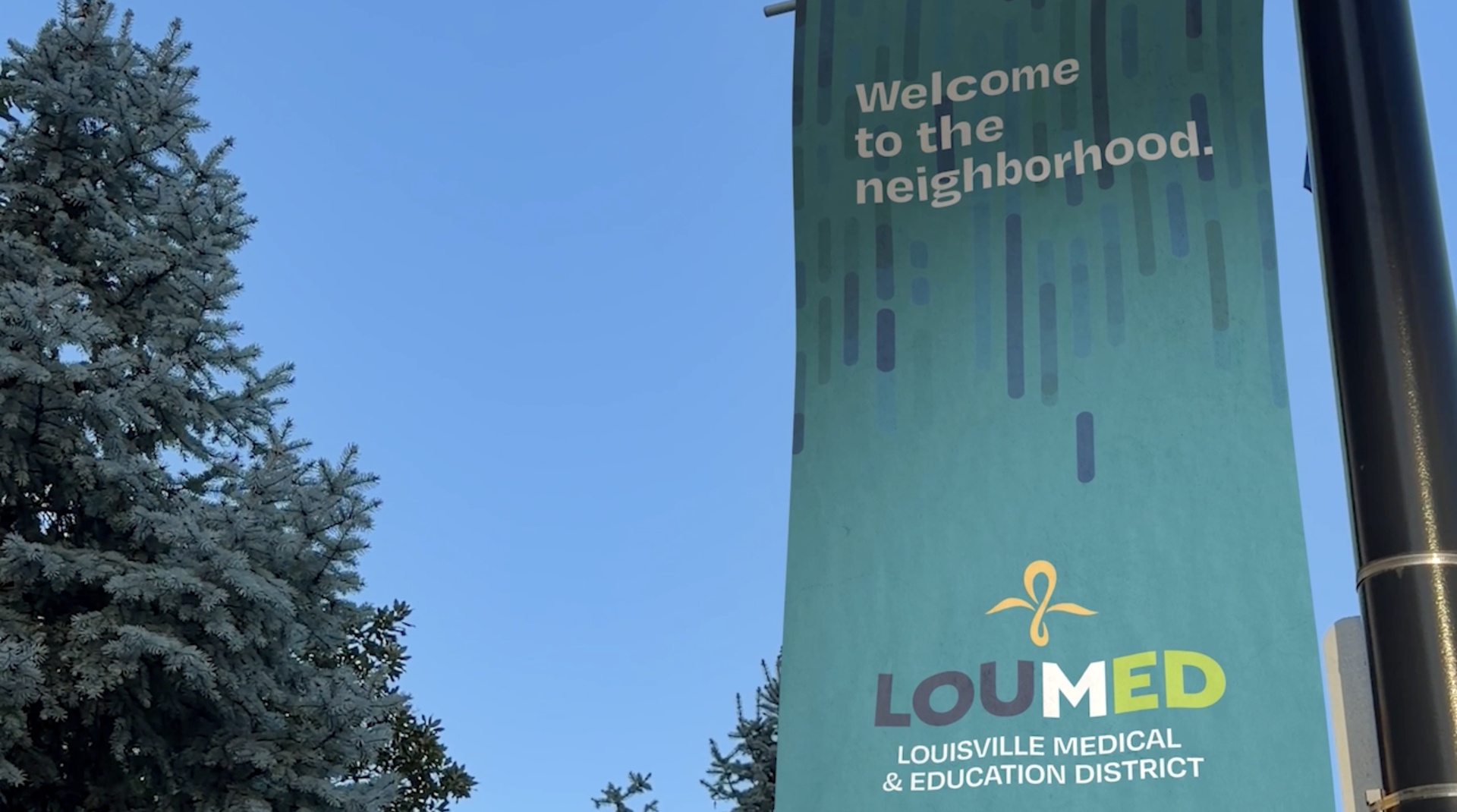 A LOUMED street banner against a blue sky, reading