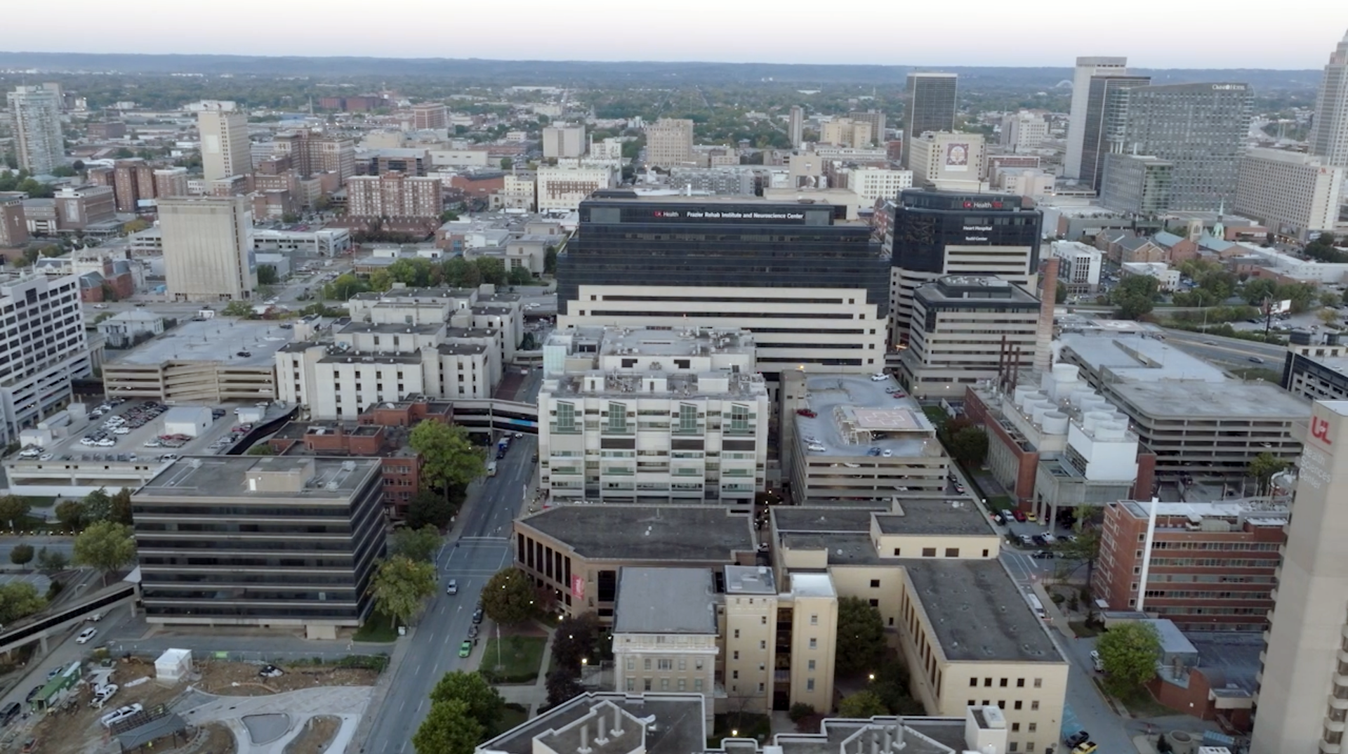Aerial view of LOUMED featuring various commercial buildings, parking structures, and city streets at dusk.