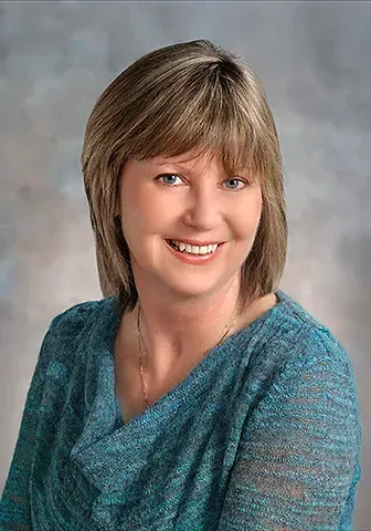 A woman in a blue shirt is smiling for the camera.