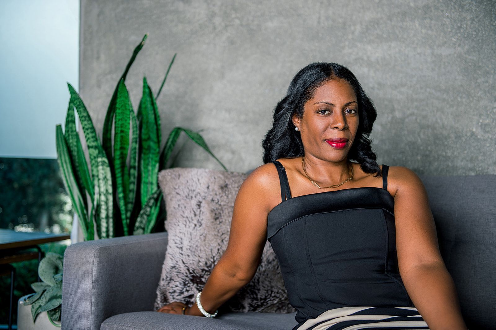 A woman is sitting on a couch in front of a plant.