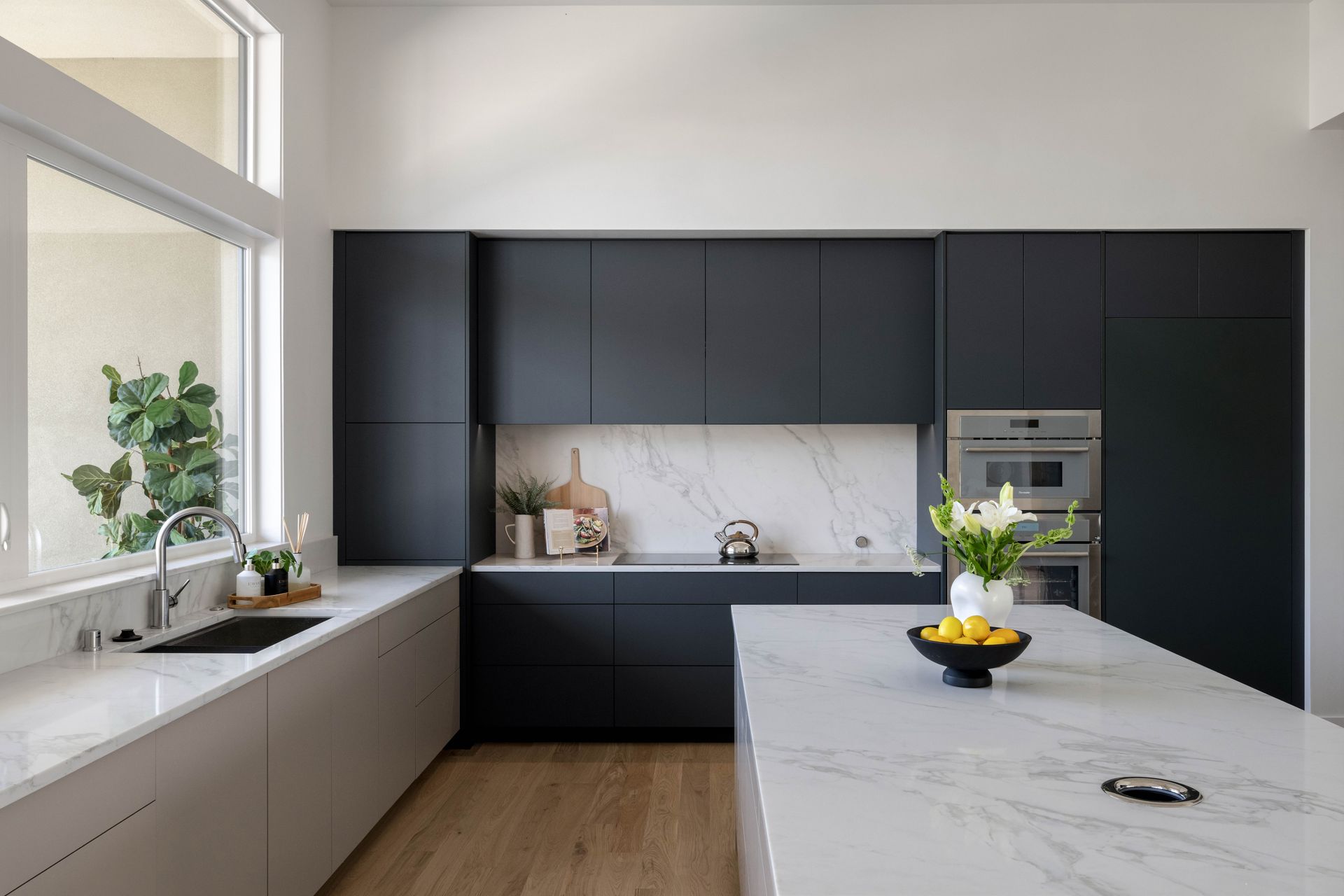 Modern kitchen with dark gray cabinets, white countertops, large window, and island with fruit.