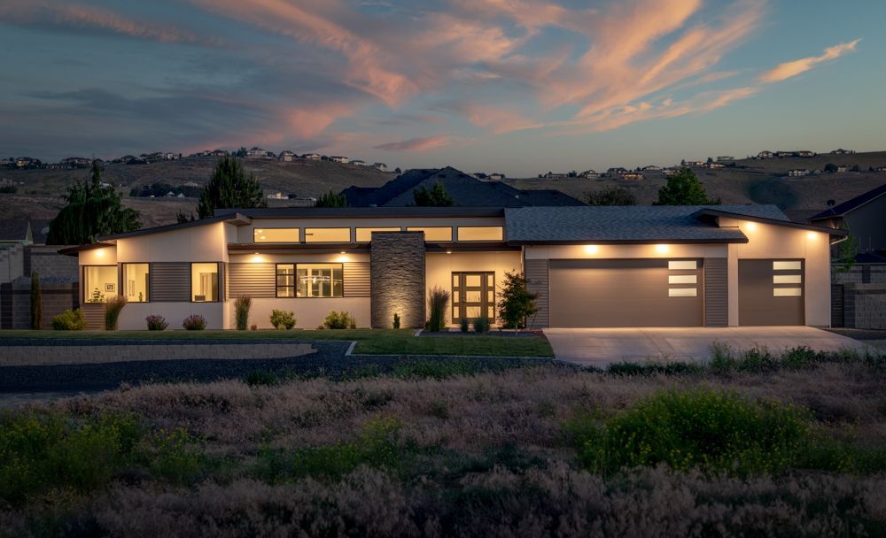 A large house is lit up at night with a sunset in the background.