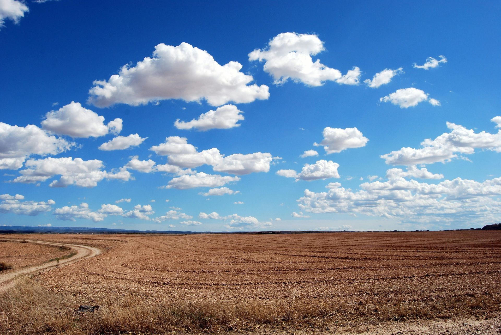 Cloud-filled blue sky over a vast, dry, brown field with a dirt path.