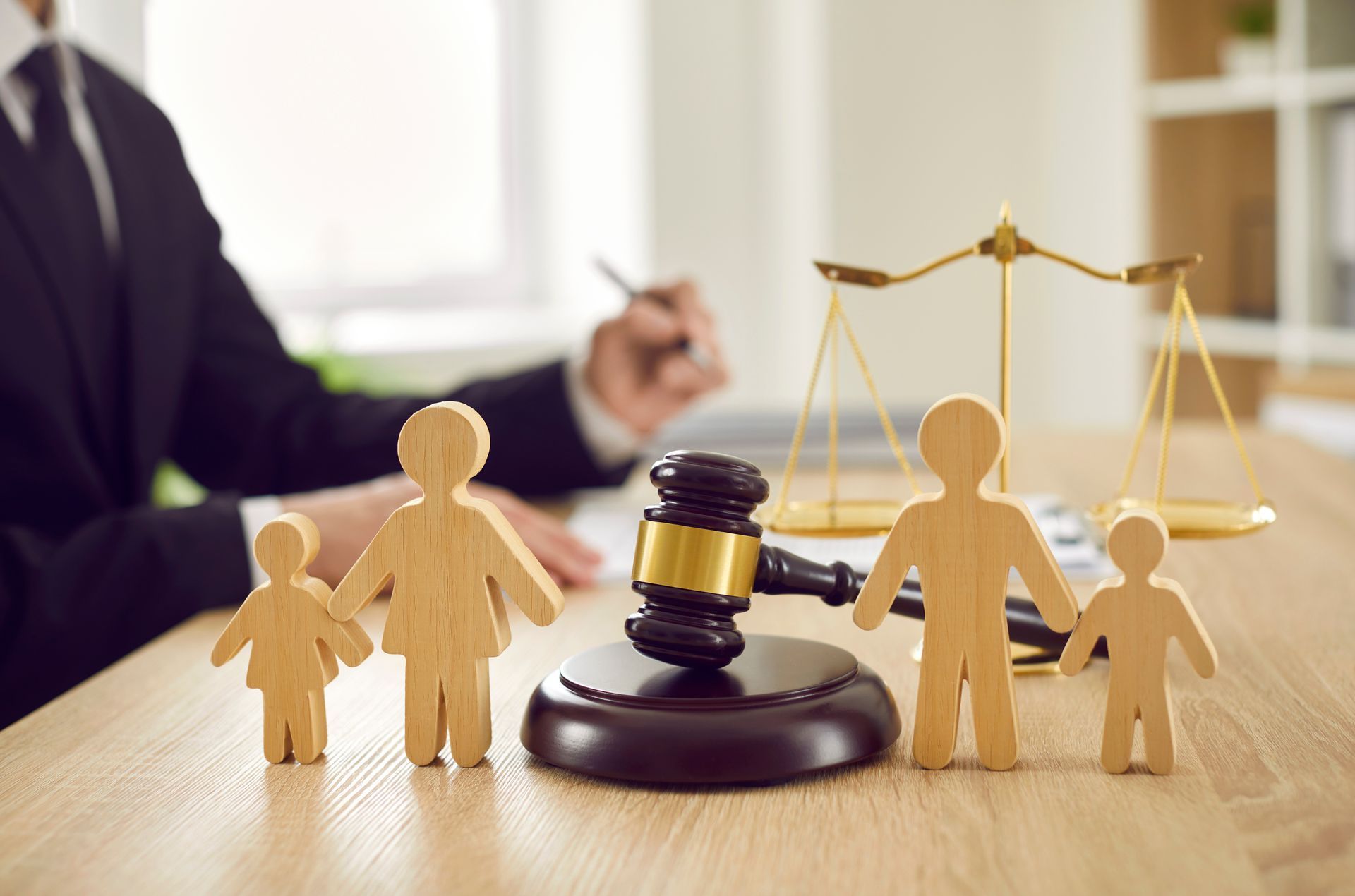 A gavel, sound block, and wooden family figures sit on a desk with justice scales in the background.