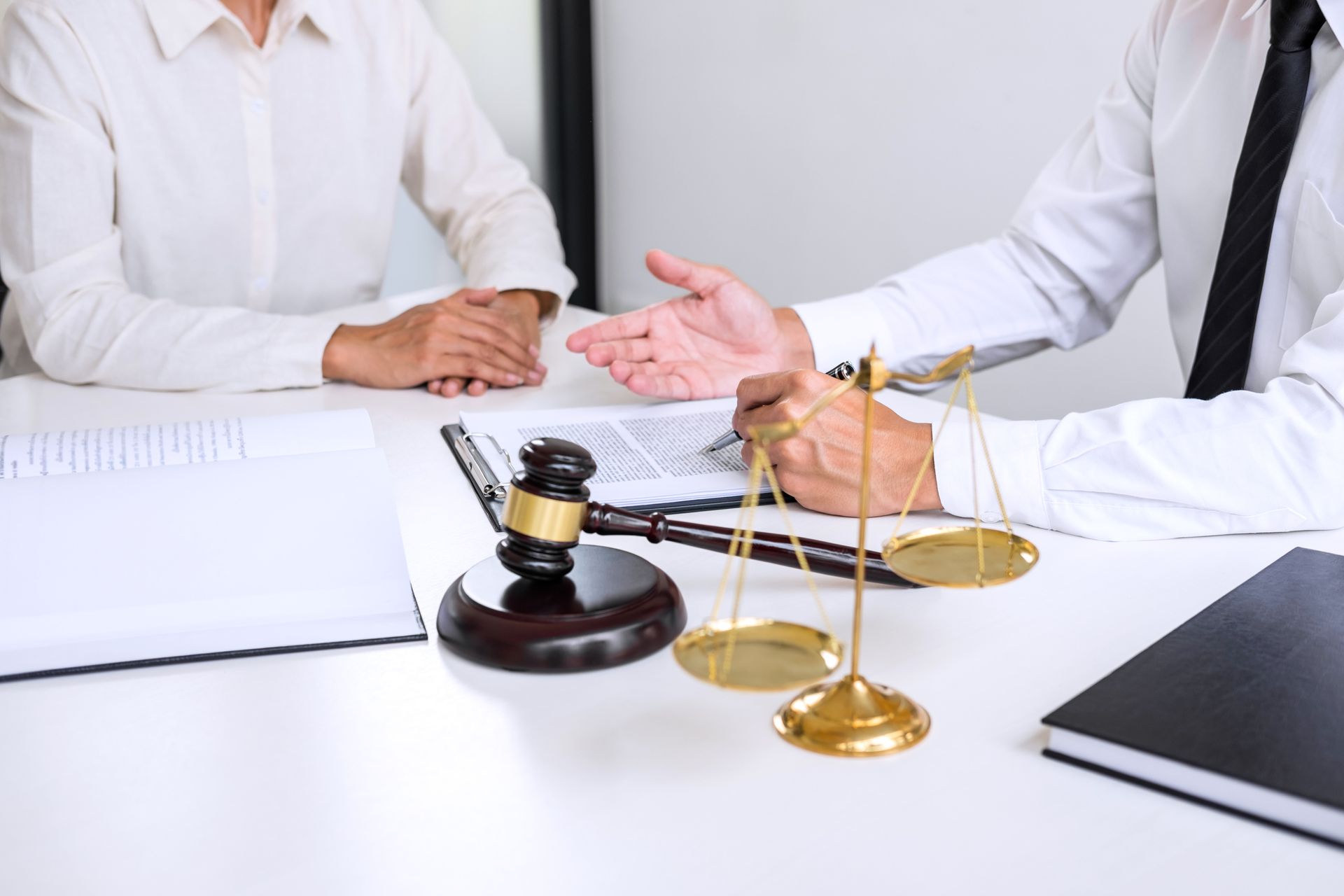 Lawyer consulting with a client at a desk; scales of justice, gavel, and documents visible.