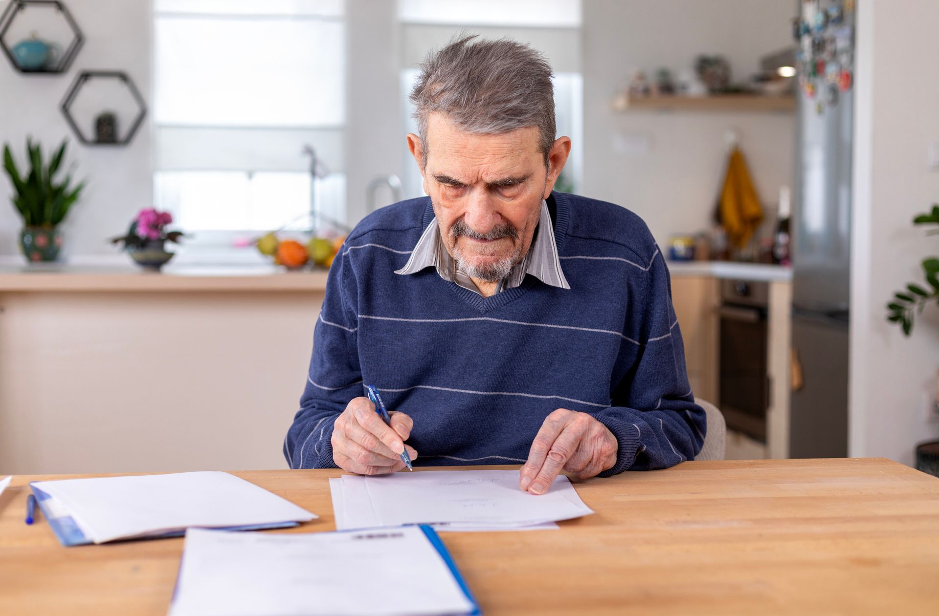 An elderly man is sitting at a table writing on a piece of paper — Monroe, MI — Apex Legal Group