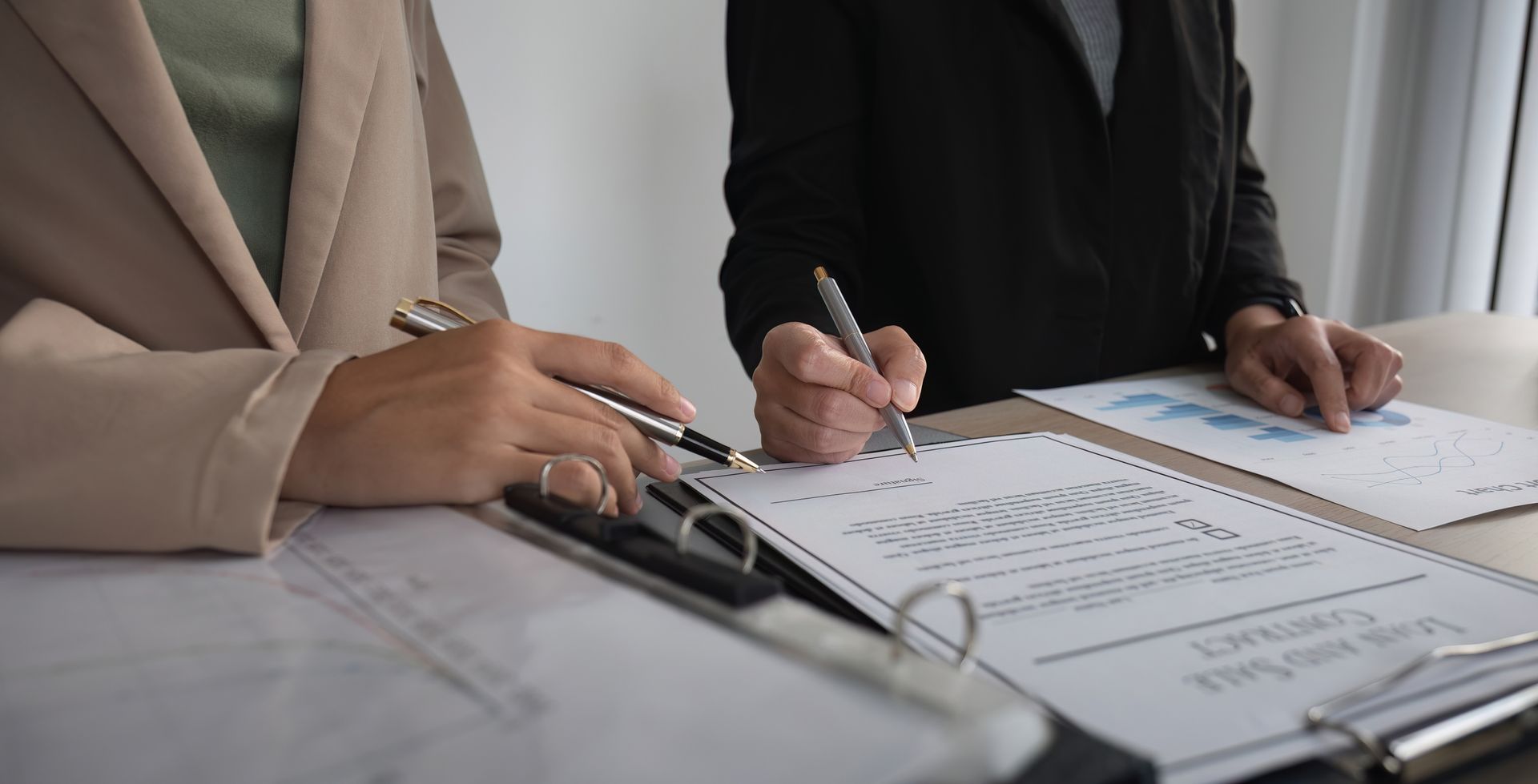 A man and a woman are sitting at a table writing on a clipboard — Monroe, MI — Apex Legal Group