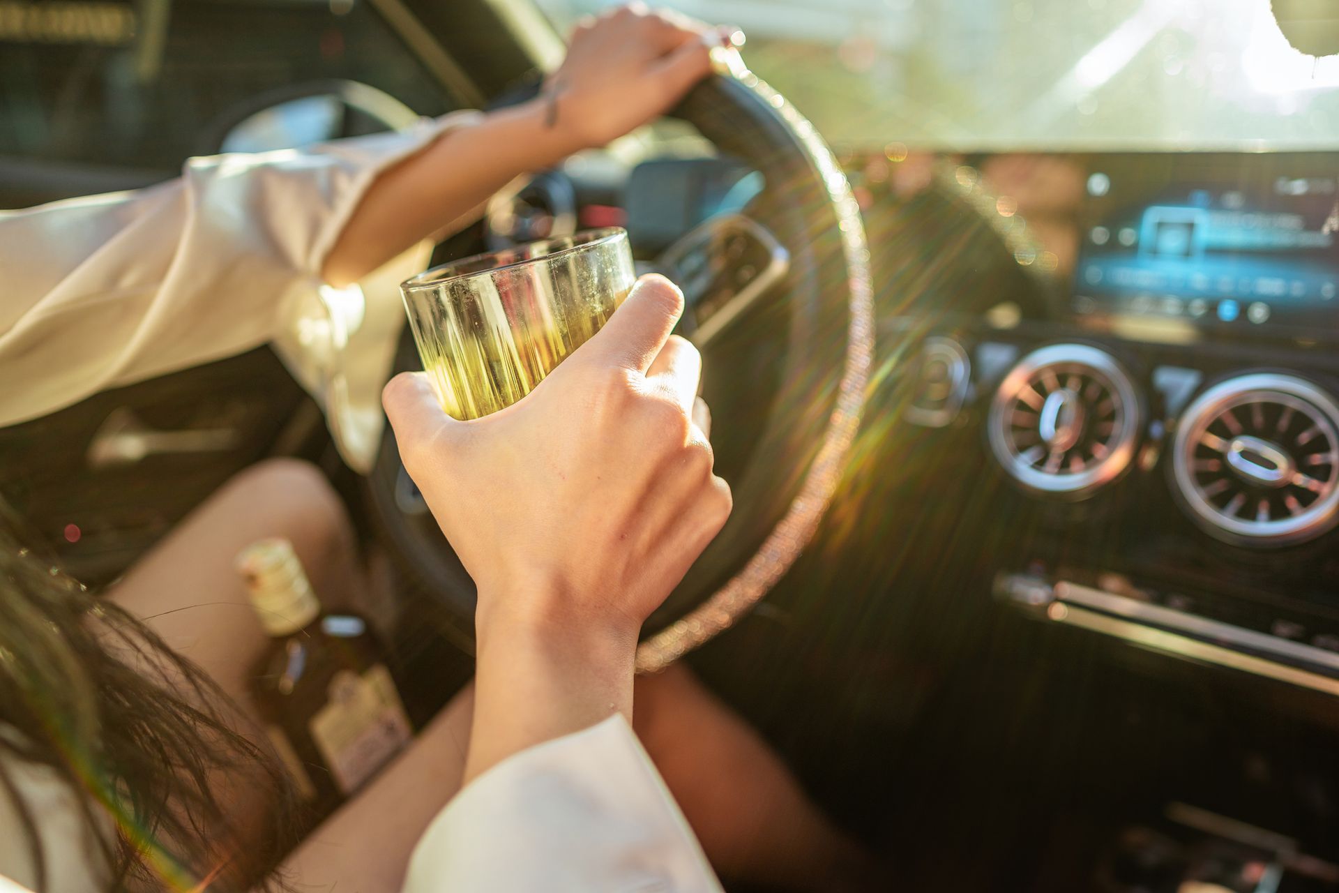 A woman is holding a glass of whiskey while driving a car — Monroe, MI — Apex Legal Group