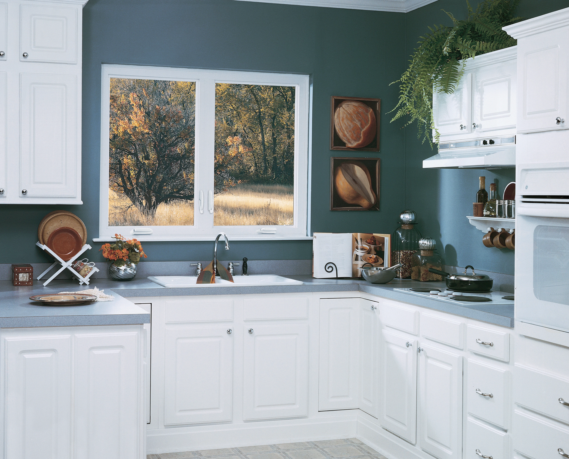 Bright white kitchen with blue-gray walls, window above sink, and decorative shelves with plants and dishes