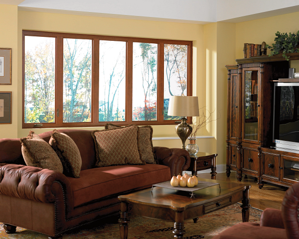 Cozy living room with a brown sofa, wooden coffee table, lamp, and large windows with daylight.