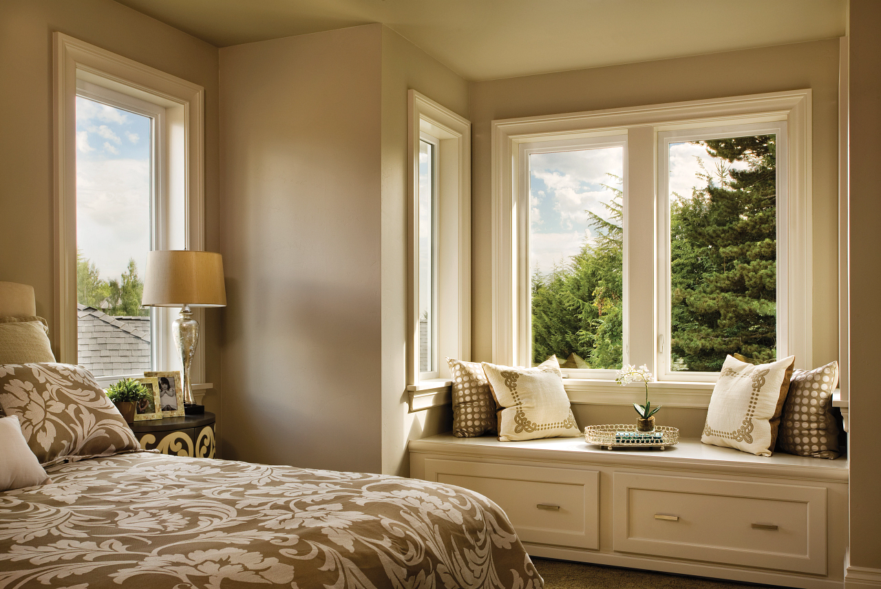 Cozy bedroom with a bed, window seat, and large sunlit windows overlooking greenery