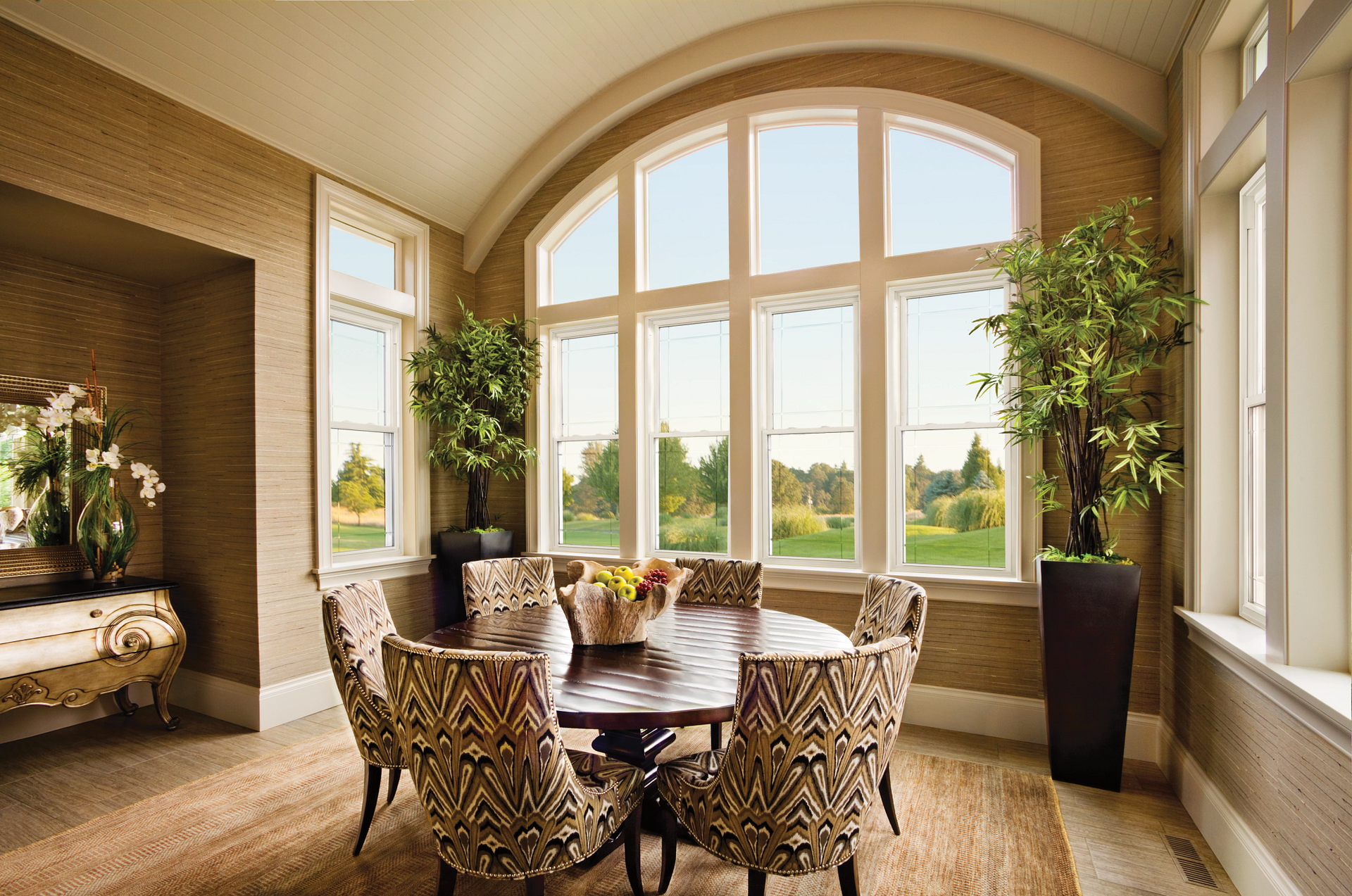 Elegant sunlit dining room with arched windows, wicker chairs, round table, and potted plants