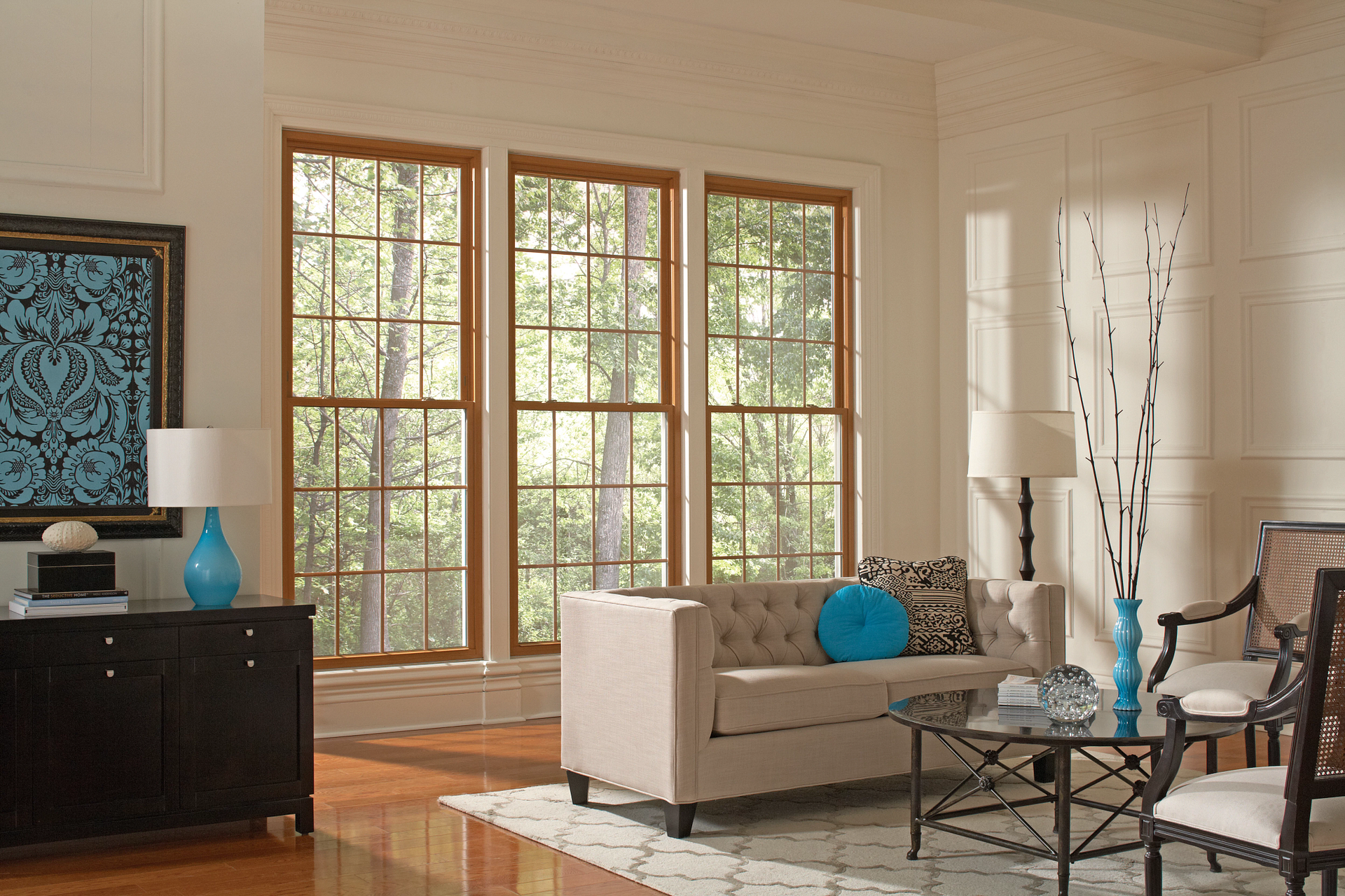 Bright living room with large windows, a beige sofa, black cabinet, and blue decor accents