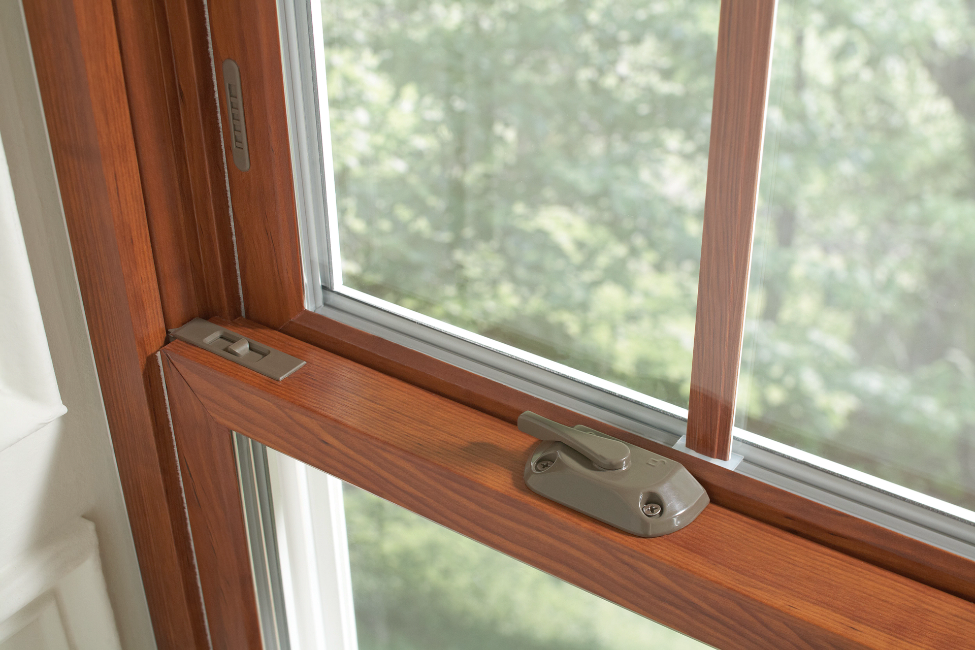Close-up of a wooden window latch and screened window frame with greenery outside