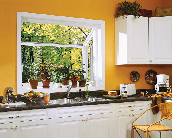 Bright kitchen with white cabinets, orange walls, black countertop, and open window overlooking green trees.