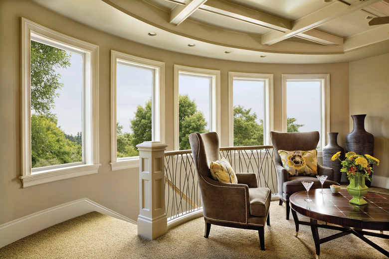 Bright sunroom with large windows, beige seating, and a round table with flowers and decor.