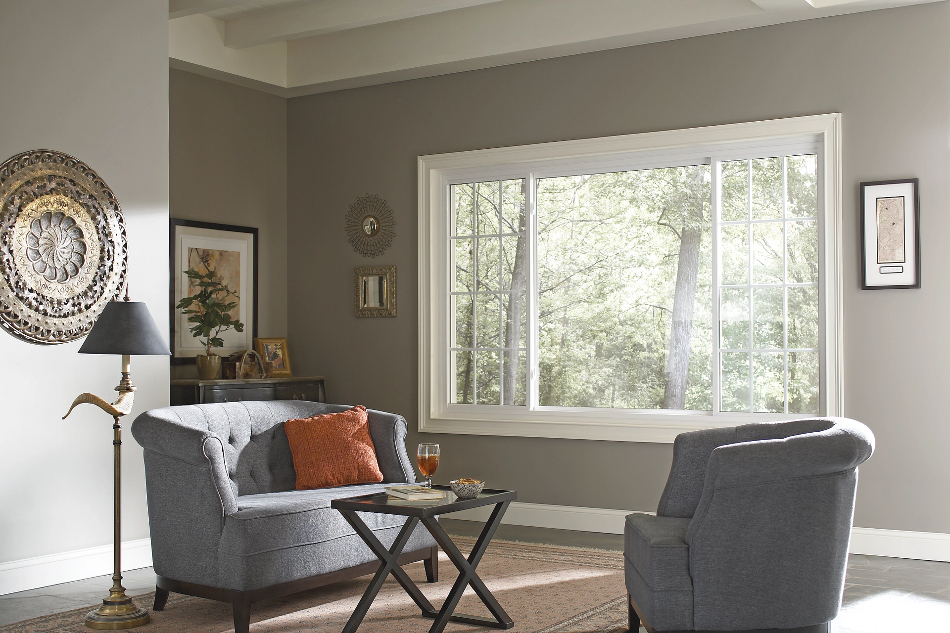Modern living room with gray chairs, orange pillow, and large window overlooking trees.
