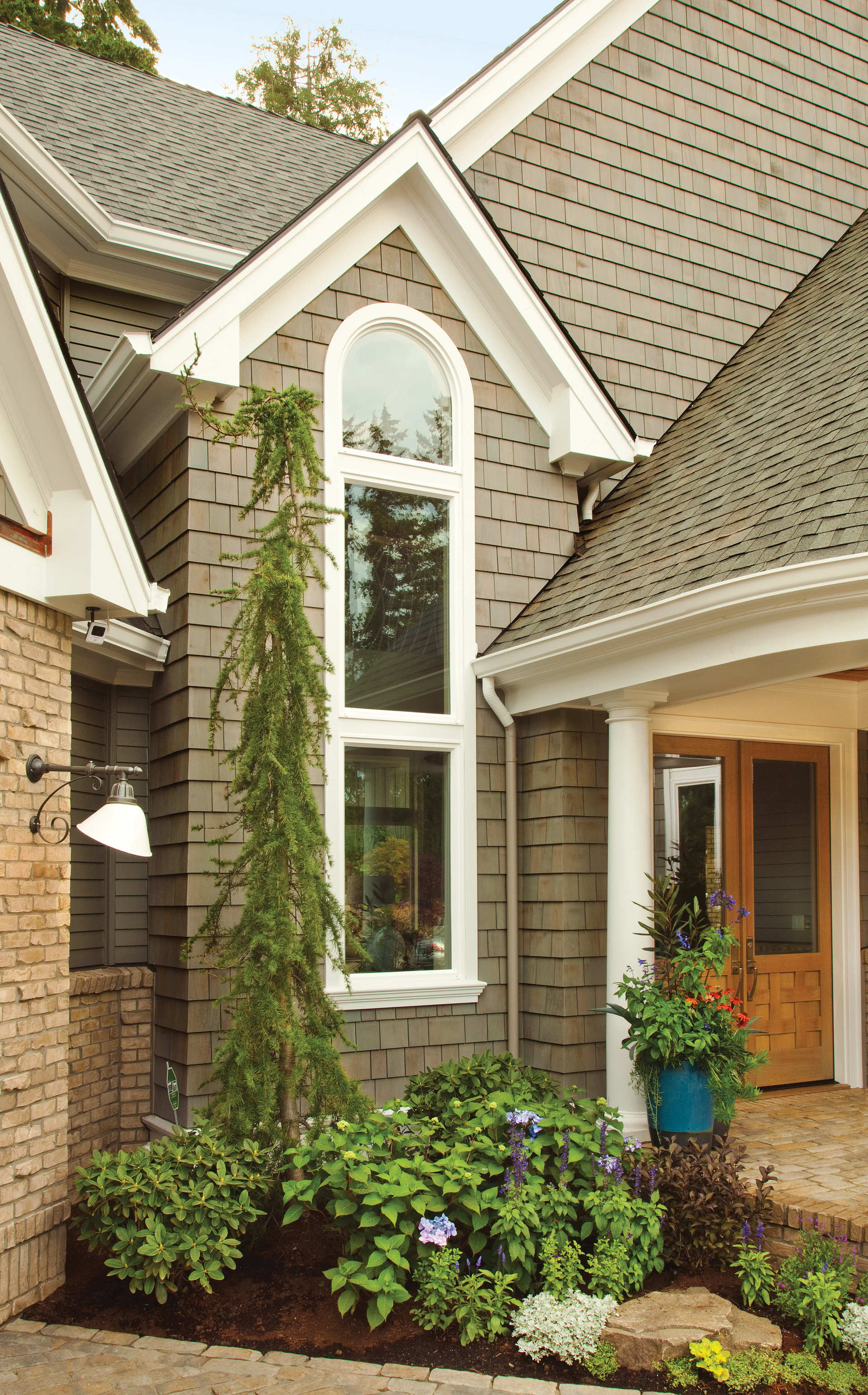 Front entry of a house with a tall arched window, beige siding, stone trim, and potted plants by the door
