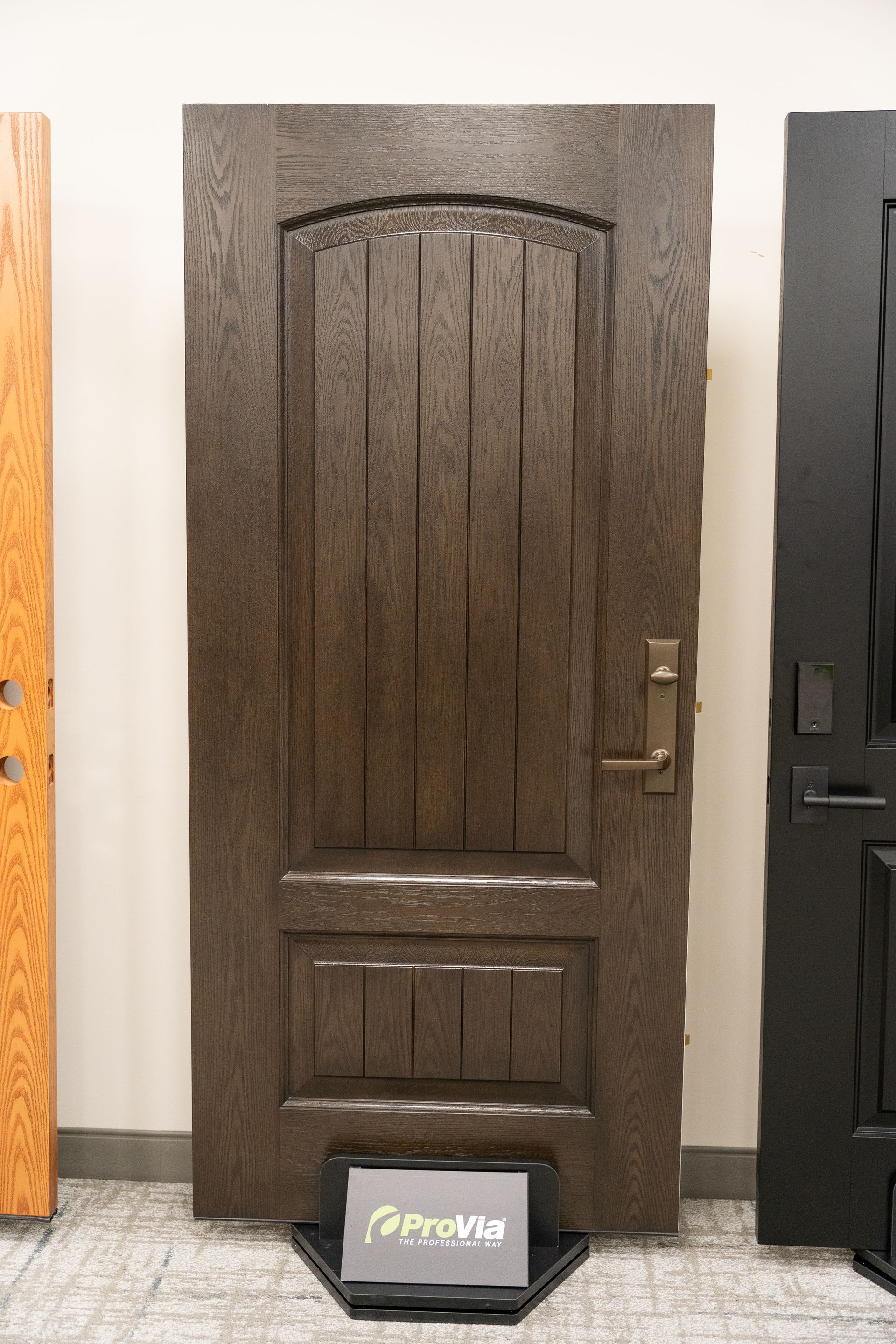 Brown decorative wooden door on display with a small sign at the bottom, flanked by other doors.