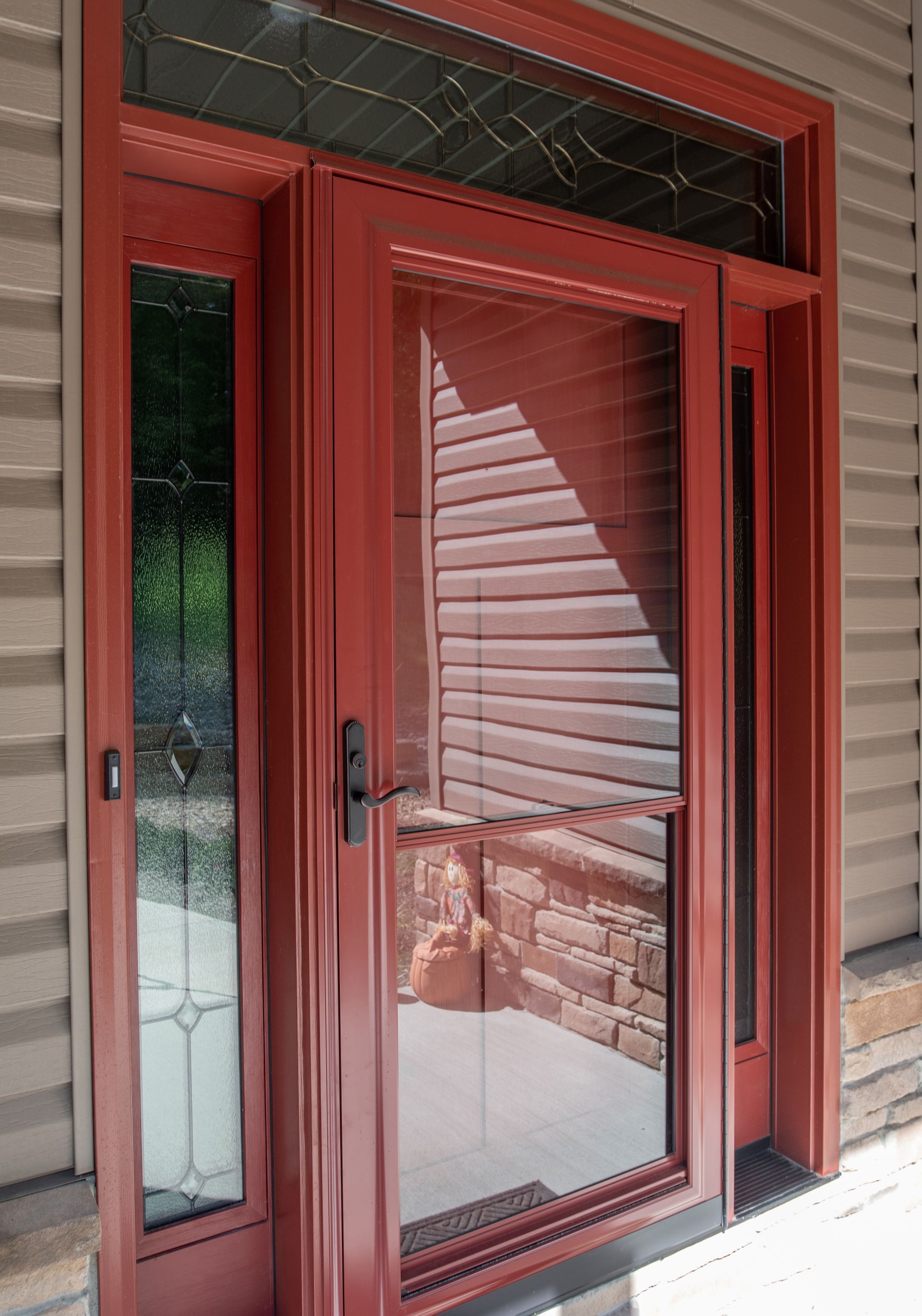 Red front door with glass side panel and reflection of porch railing and blinds