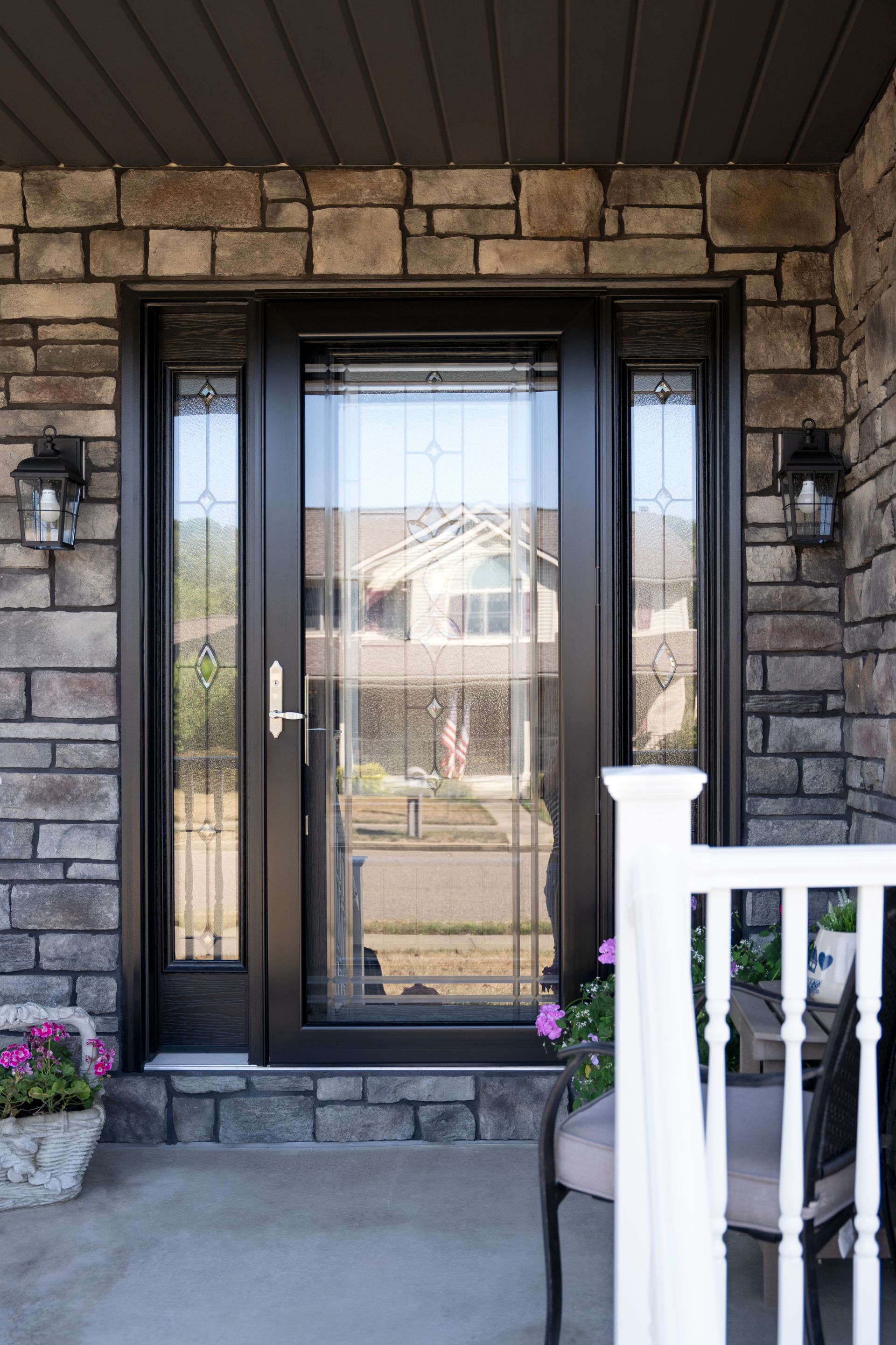Front entry with black glass door, stone facade, and white porch railing.