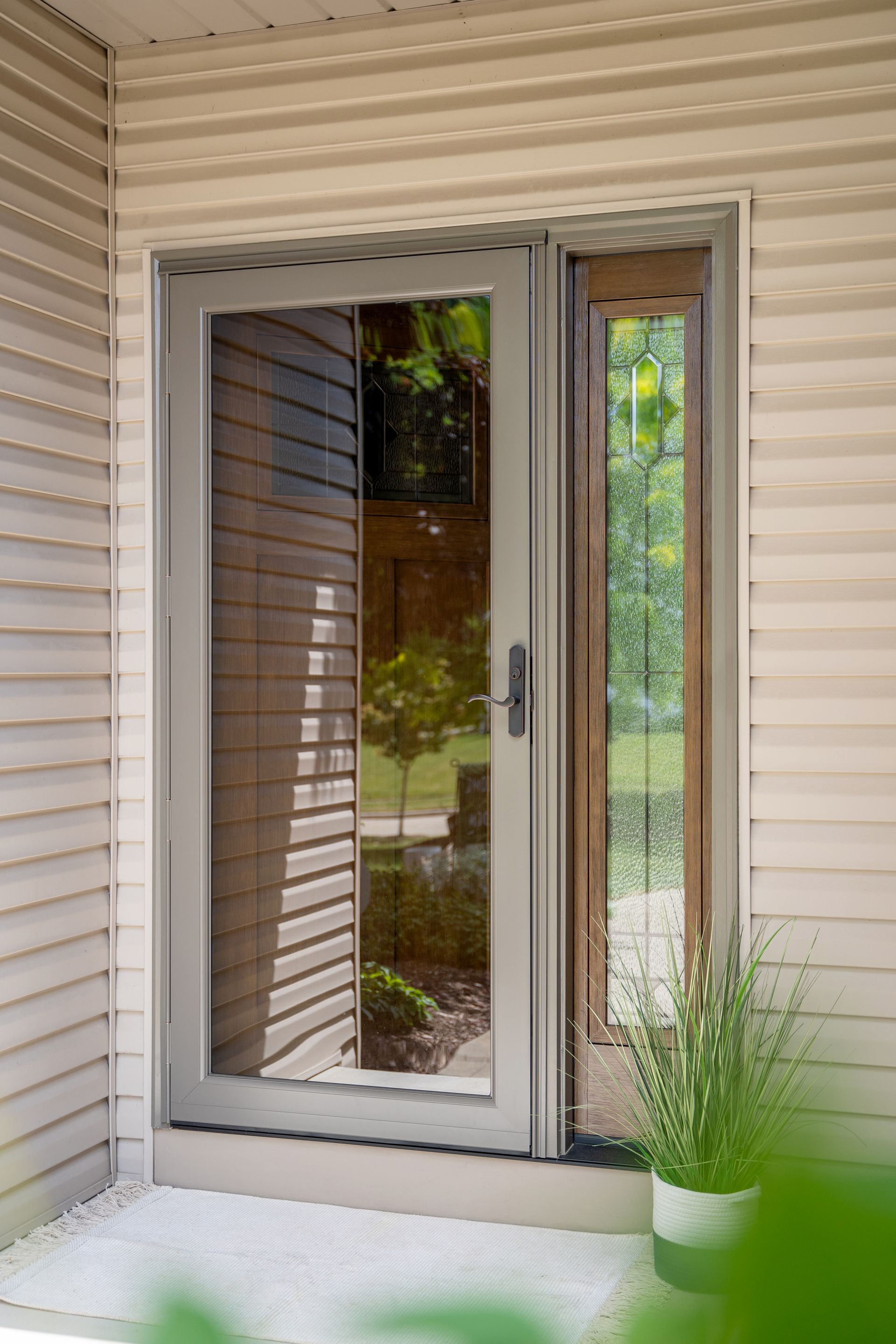 Sliding glass door with screen on a beige siding exterior, next to a small potted plant.